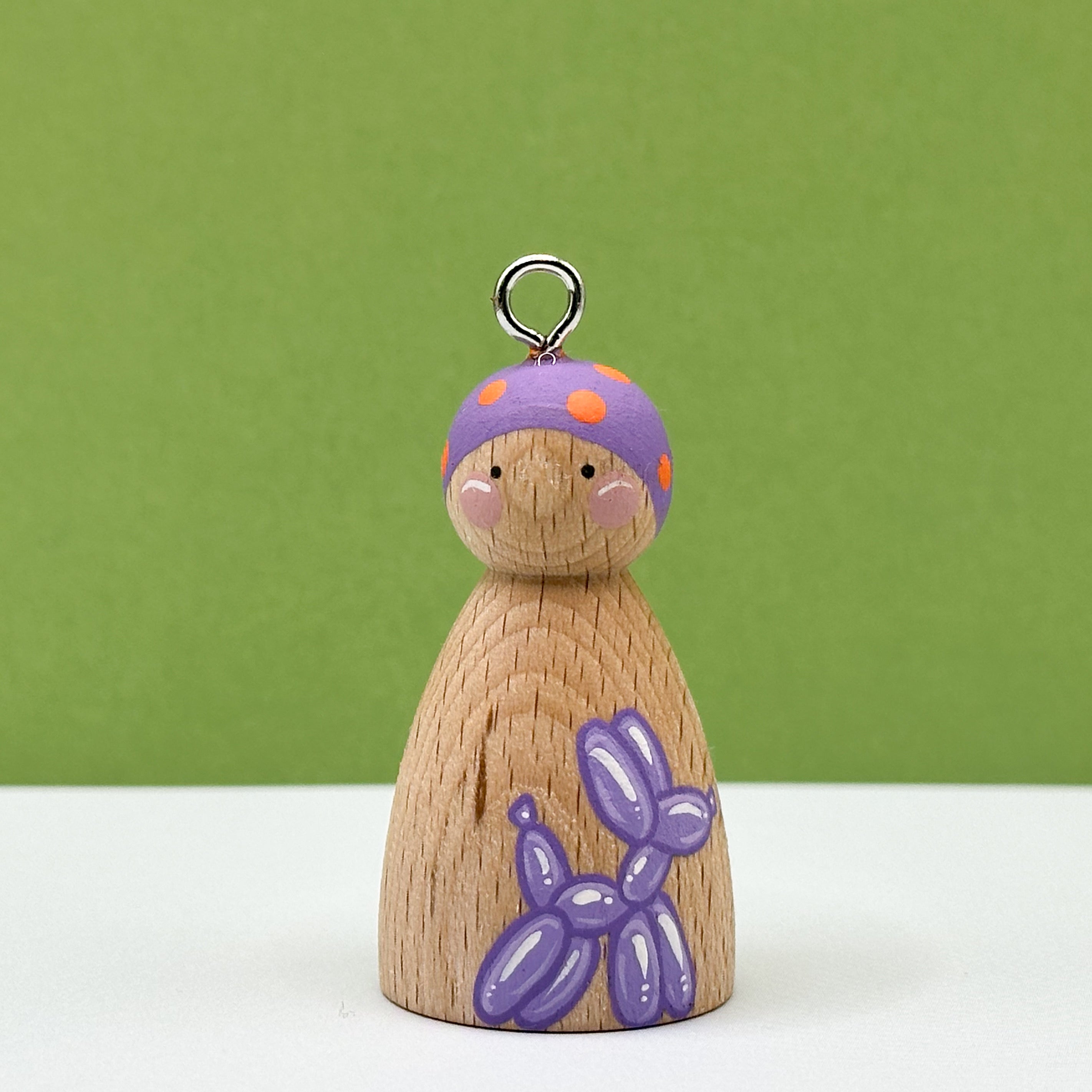 Wooden peg doll with a purple hat and balloon dog on a green background