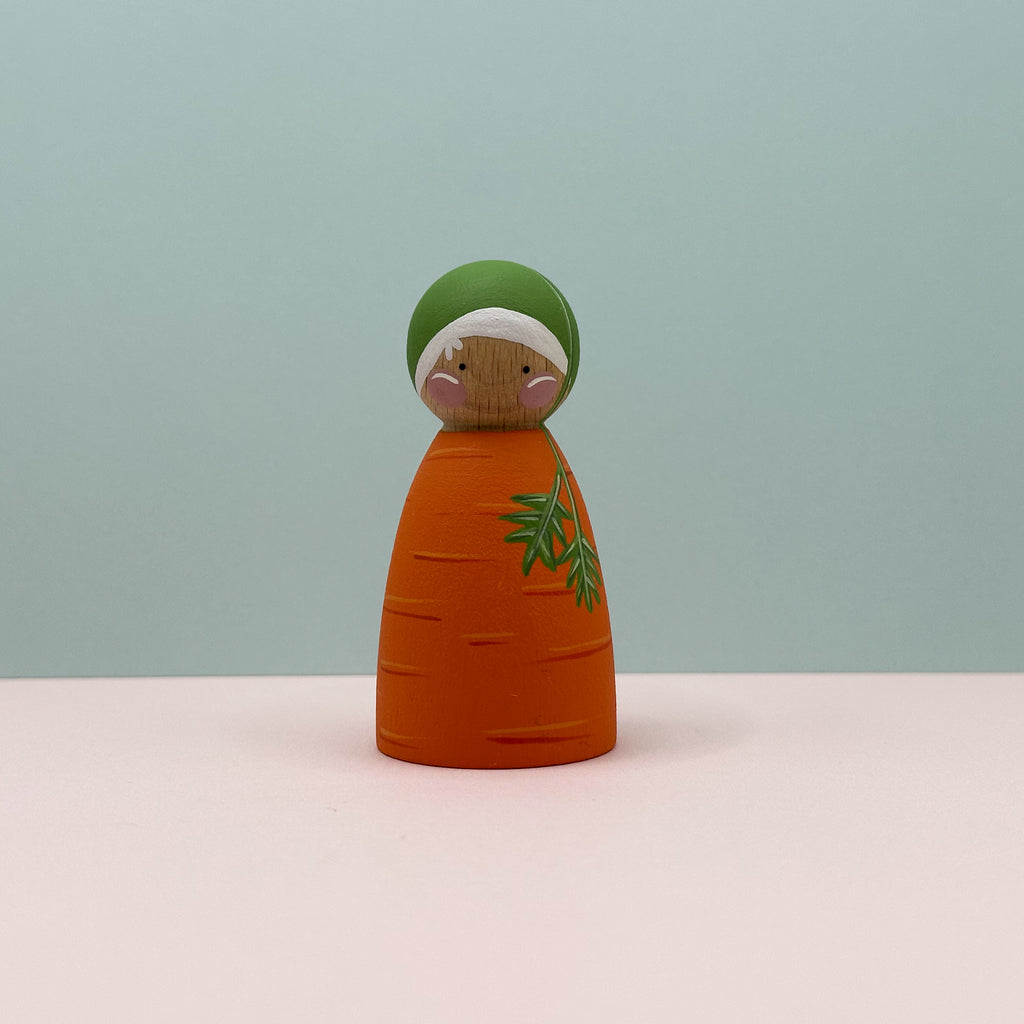 Wooden carrot-shaped figurine with a green top on a light blue background