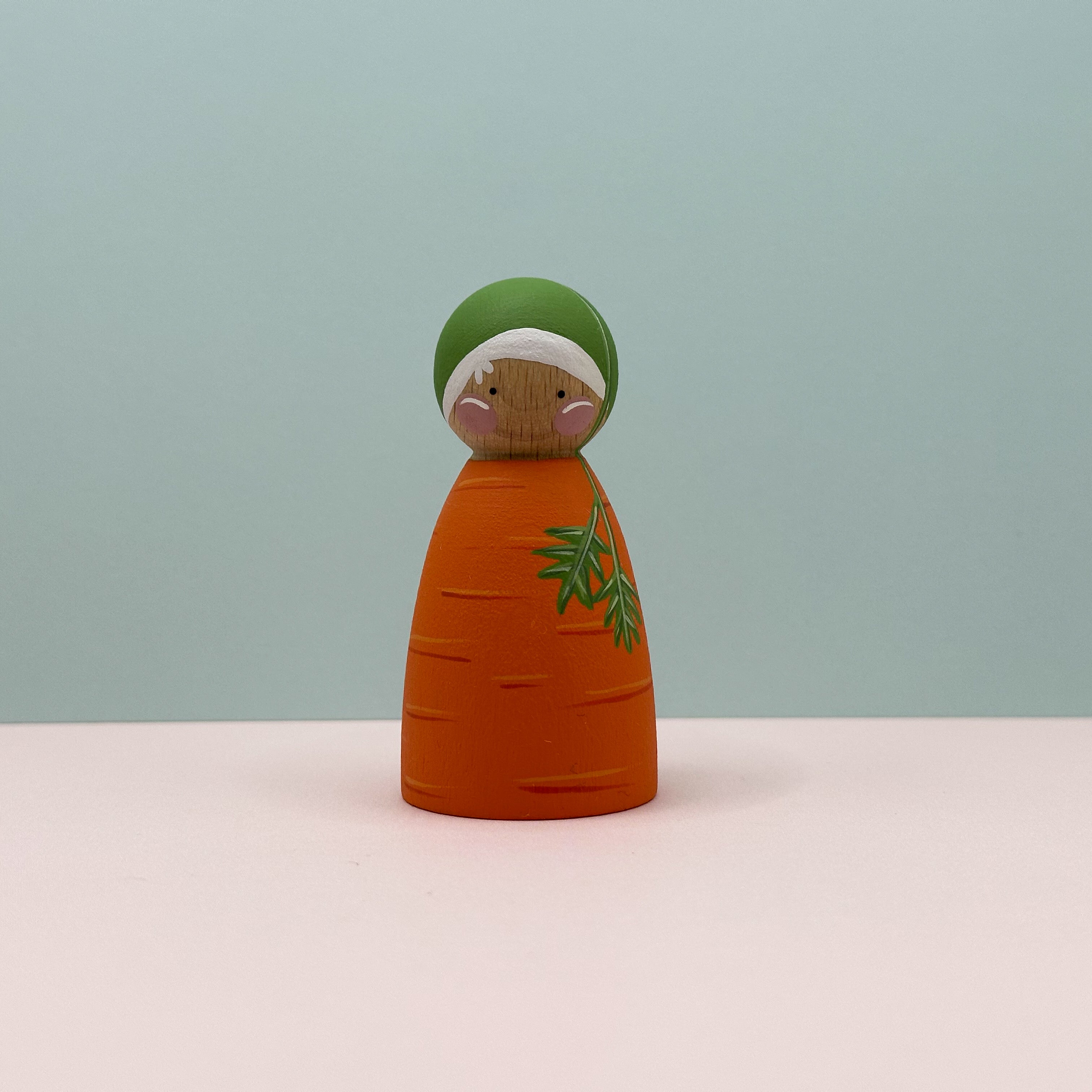 Wooden carrot-shaped figurine with a green top on a light blue background