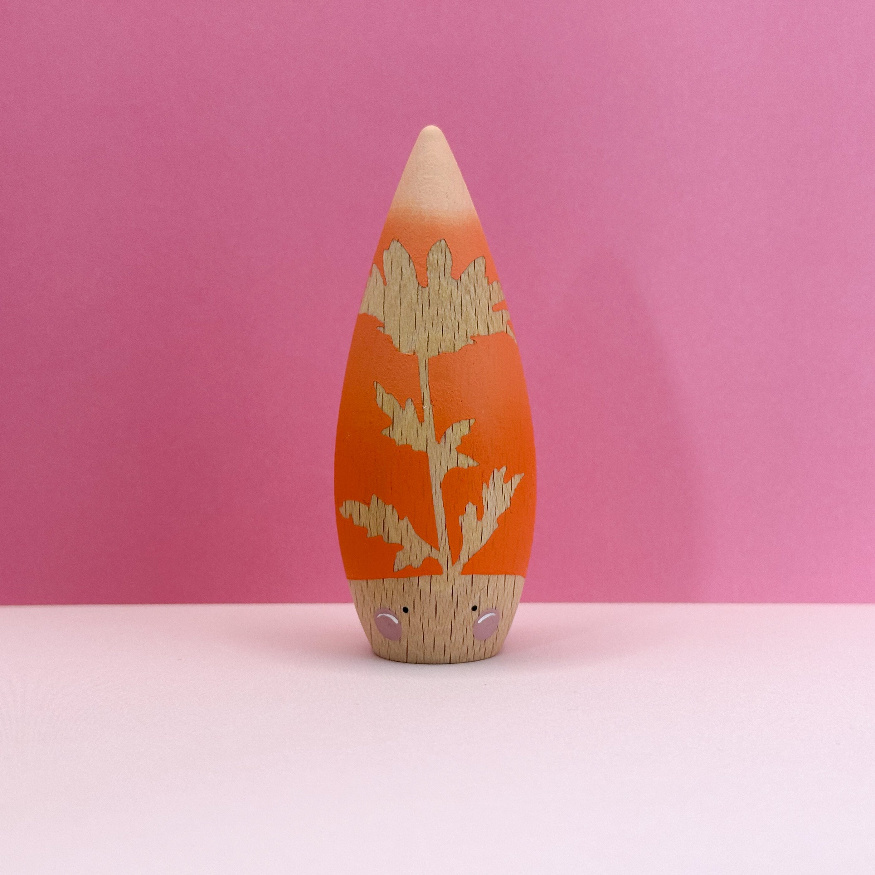 Wooden  toy with a leaf design on an orange body against a pink background
