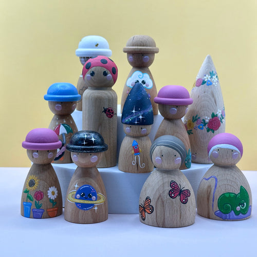 Set of wooden peg dolls with colorful hats and designs on a white surface against a yellow background