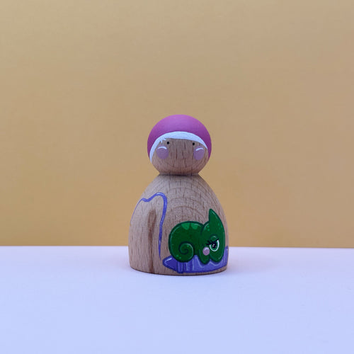 Wooden peg doll with a purple hat and green lizard design on a beige background
