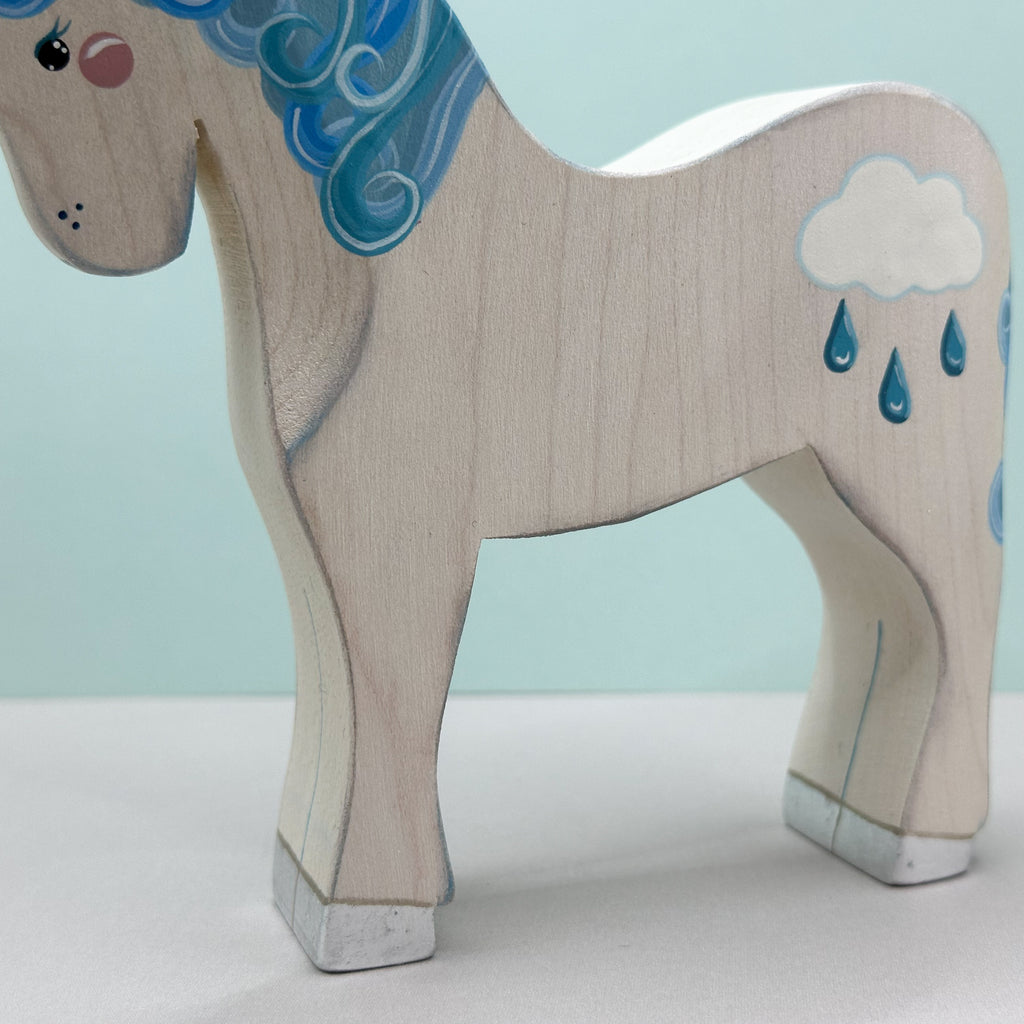 Wooden horse figurine with blue hair and cloud design on a light blue background