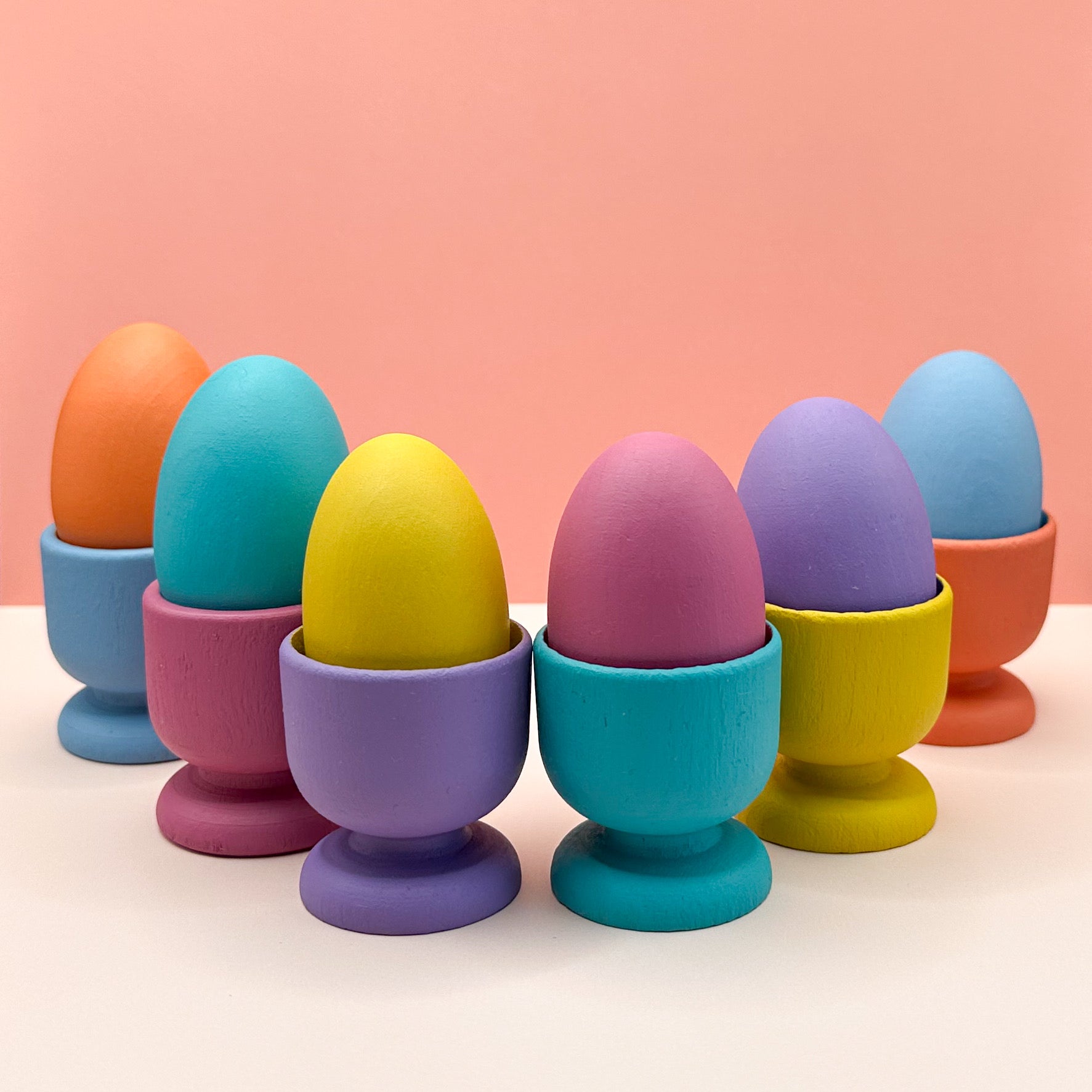 Colorful eggs in matching egg cups on a peach background