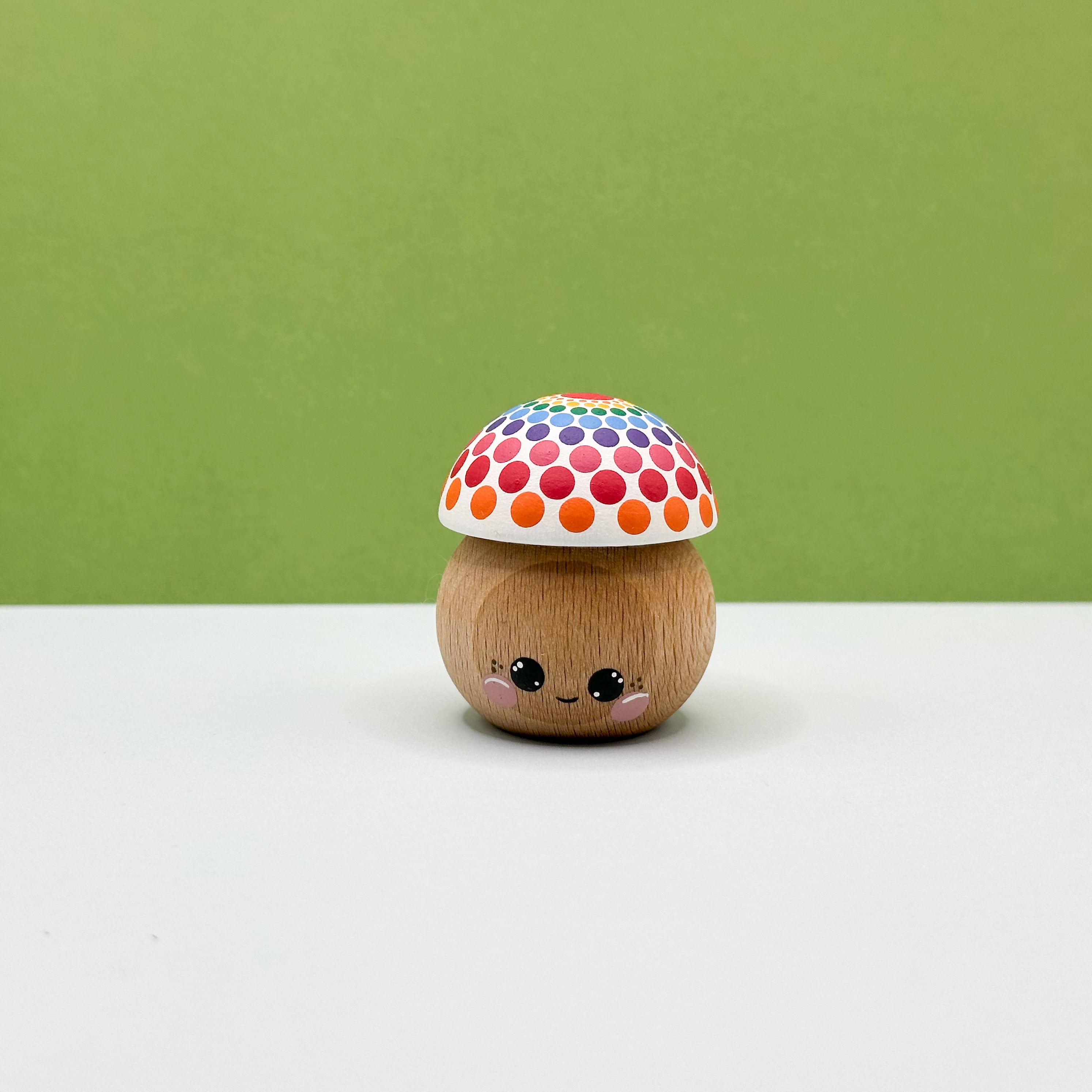 Wooden toy mushroom with a colorful polka dot cap on a white surface with a green background