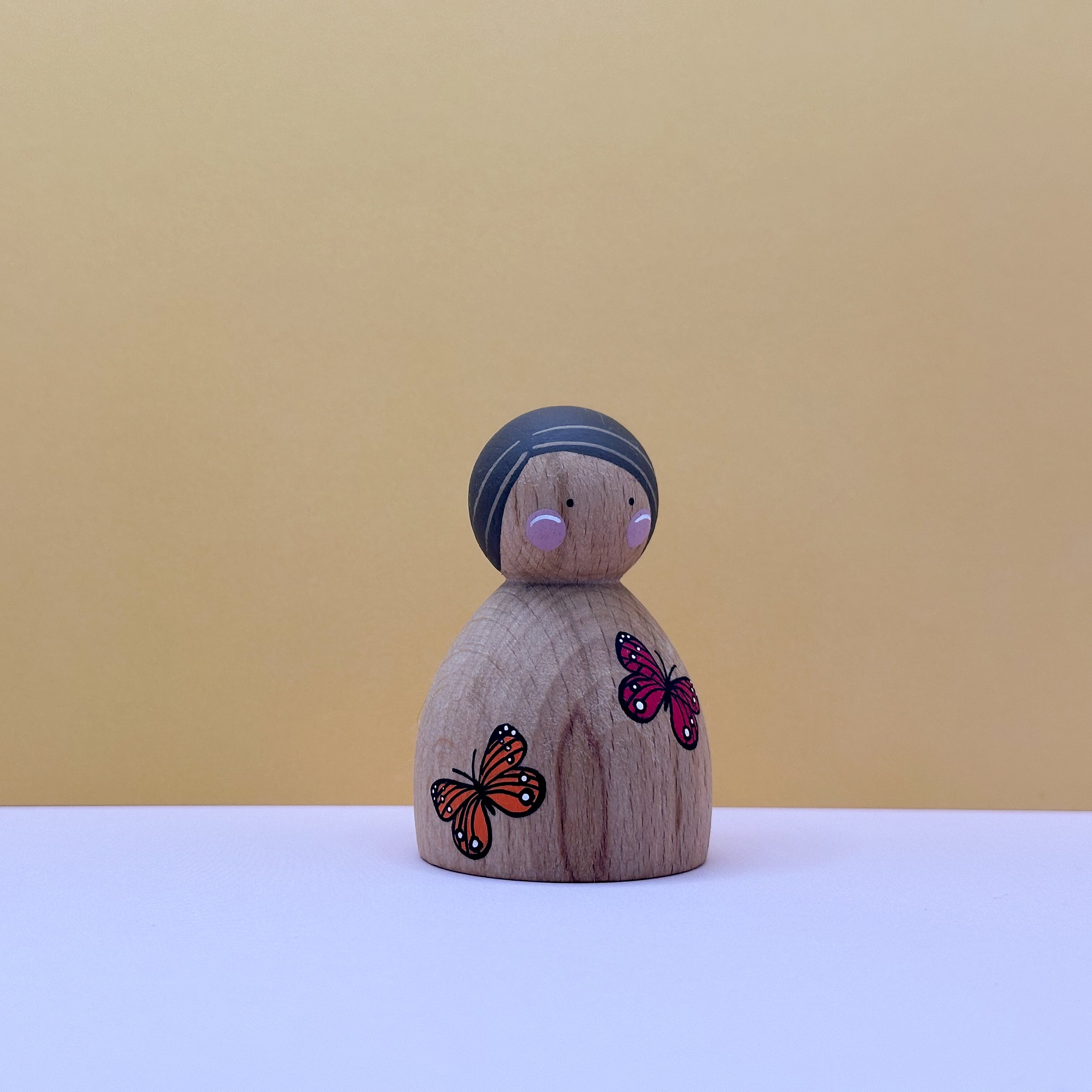 Wooden peg doll with a headband and butterfly decorations on a beige background