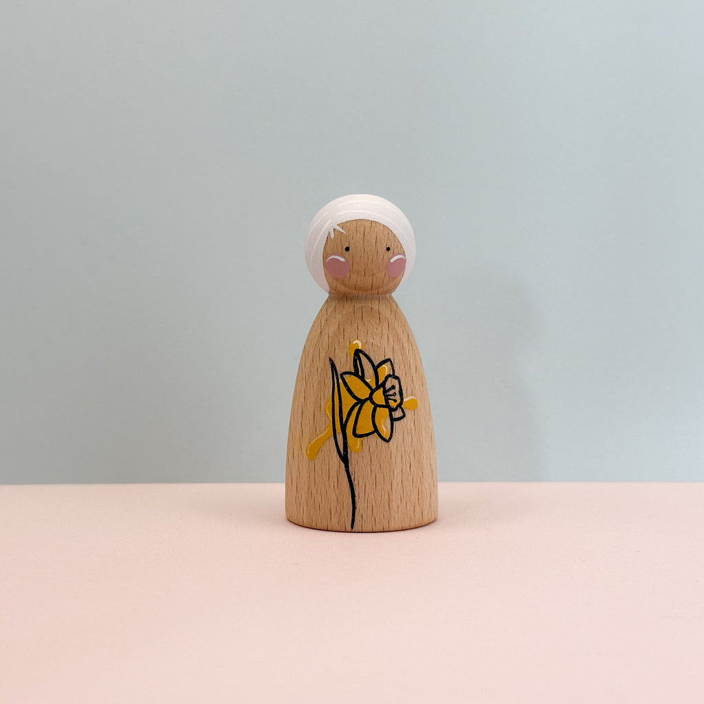 Wooden peg doll with a daffodil design on a light gray background