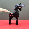 Black unicorn figurine with a pink heart on a red surface and gray background