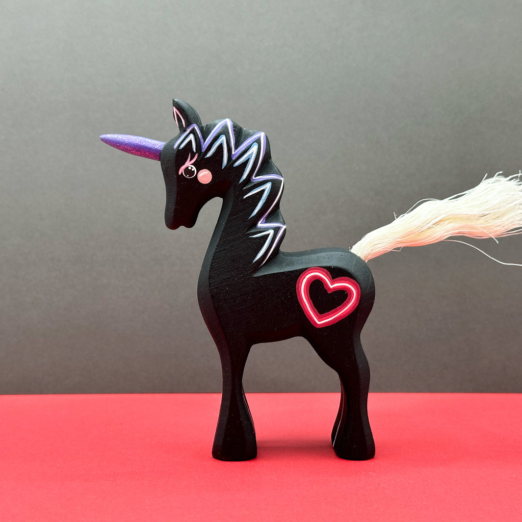 Black unicorn figurine with a pink heart on a red surface and gray background