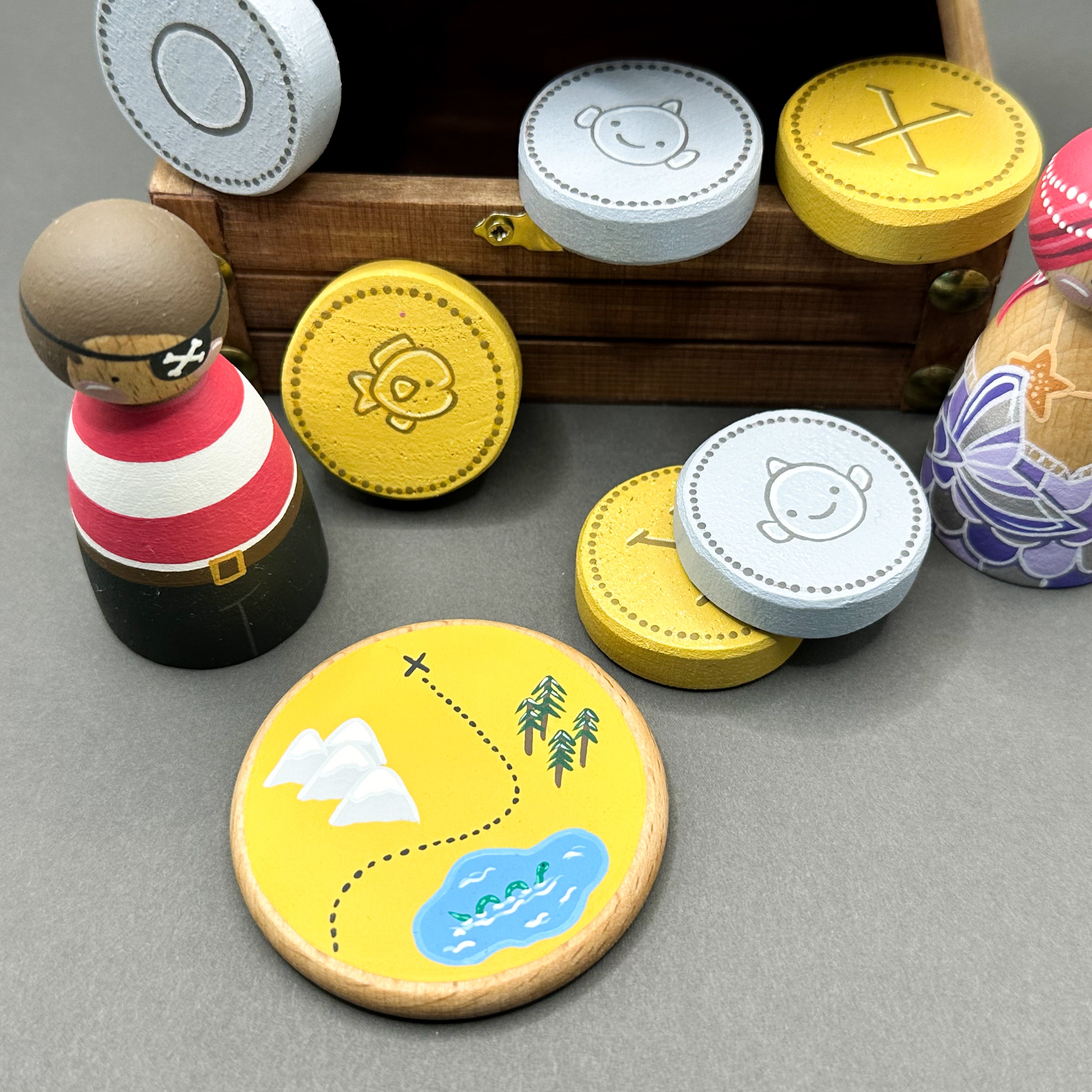 Wooden toy treasure chest with wooden peg dolls, wooden coins and a round disc shaped treasure map