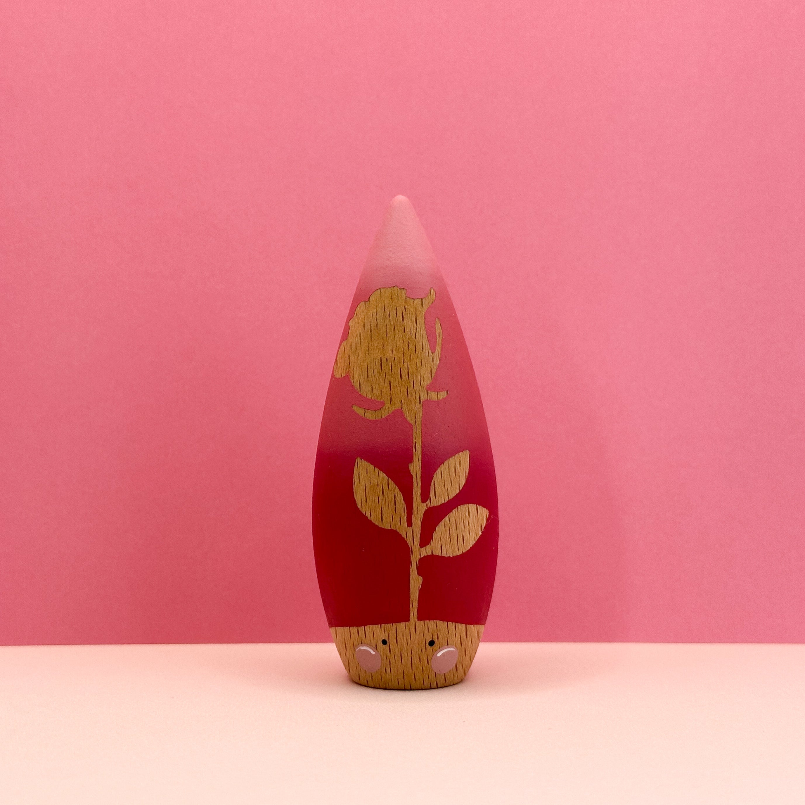 Decorative cone-shaped toy with a red base, rose design, and pink top on a pink background