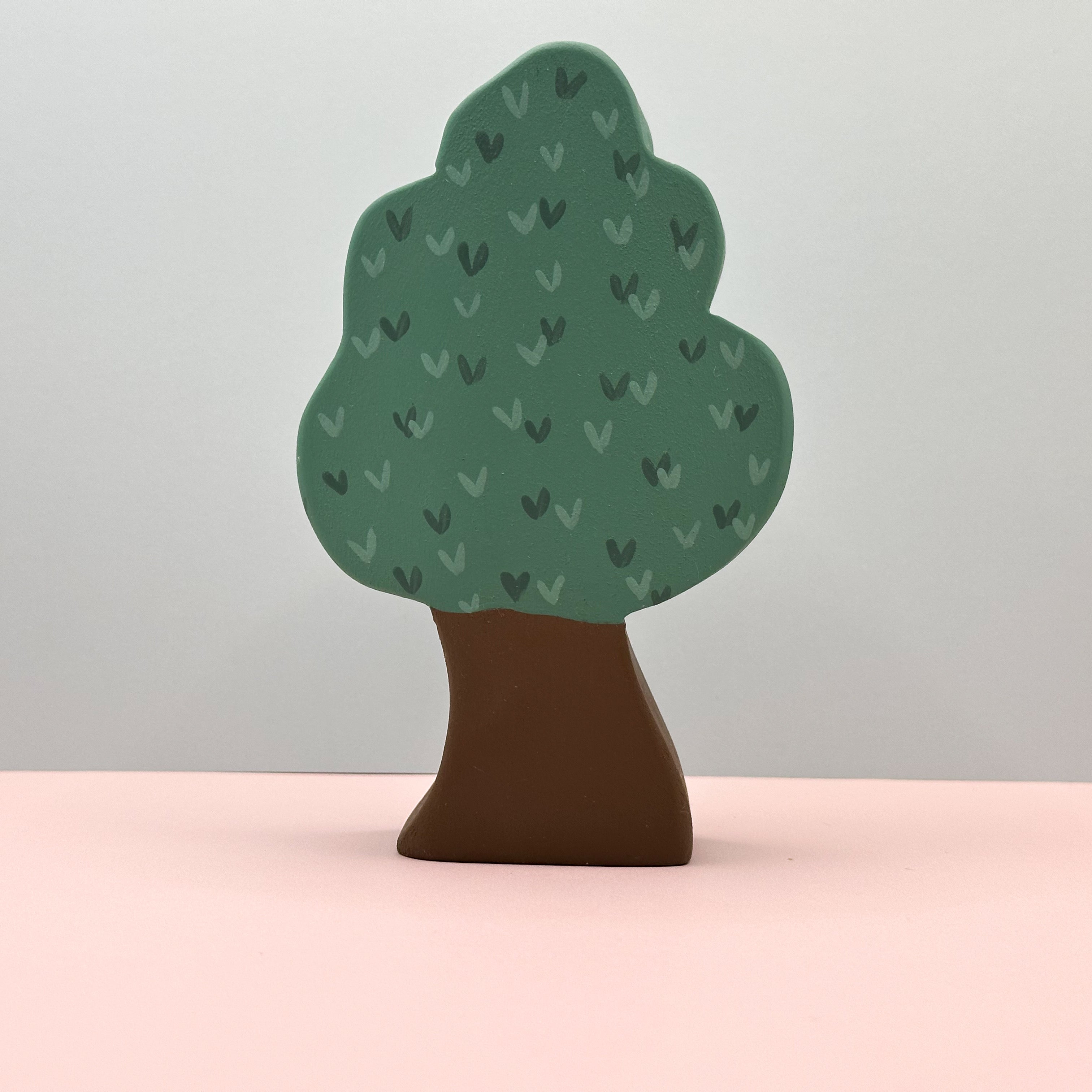 Tree-shaped object with green leaves and brown trunk on a pink surface and light gray background