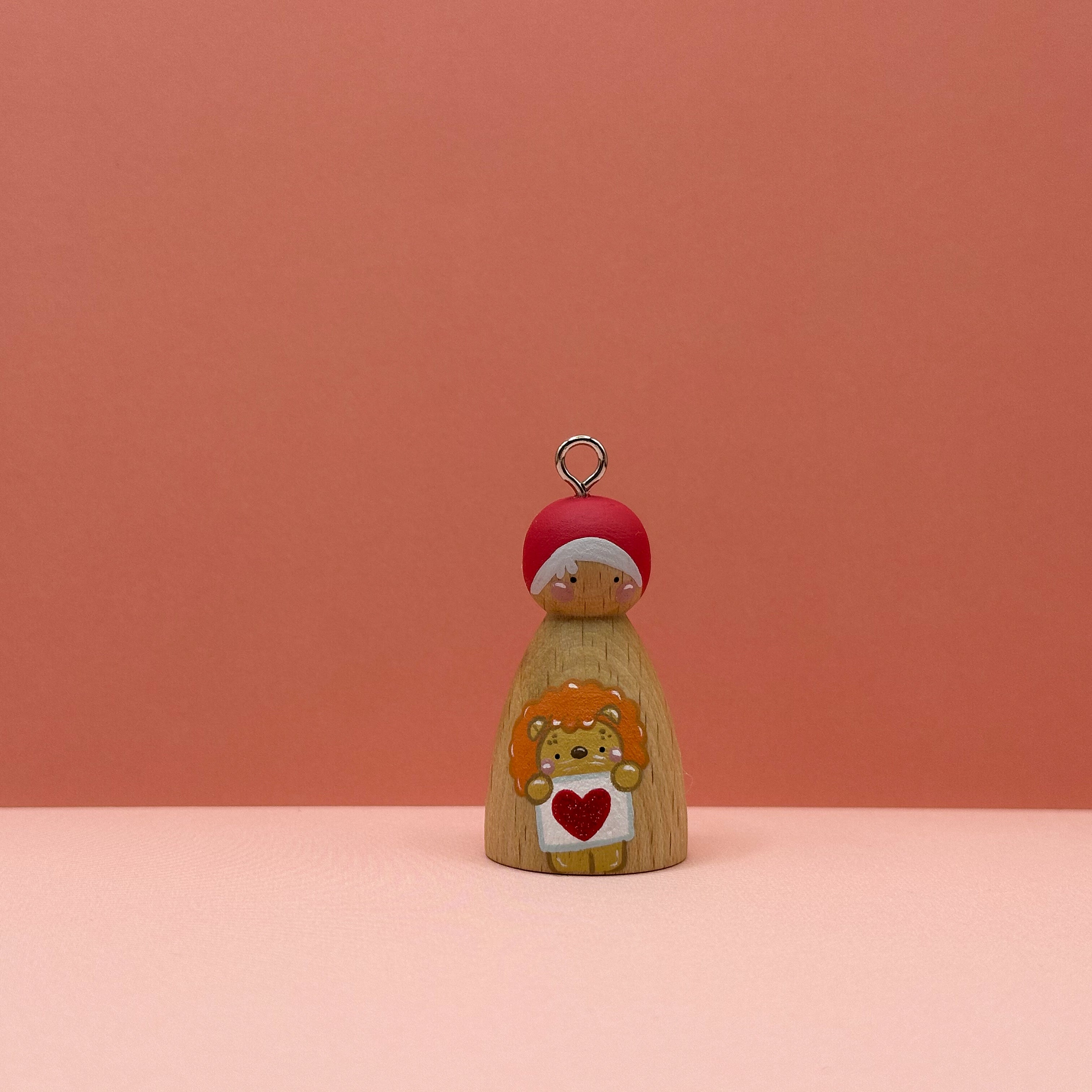 Small peg doll keyring with a lion holding a heart sign painted on its body with a peach background