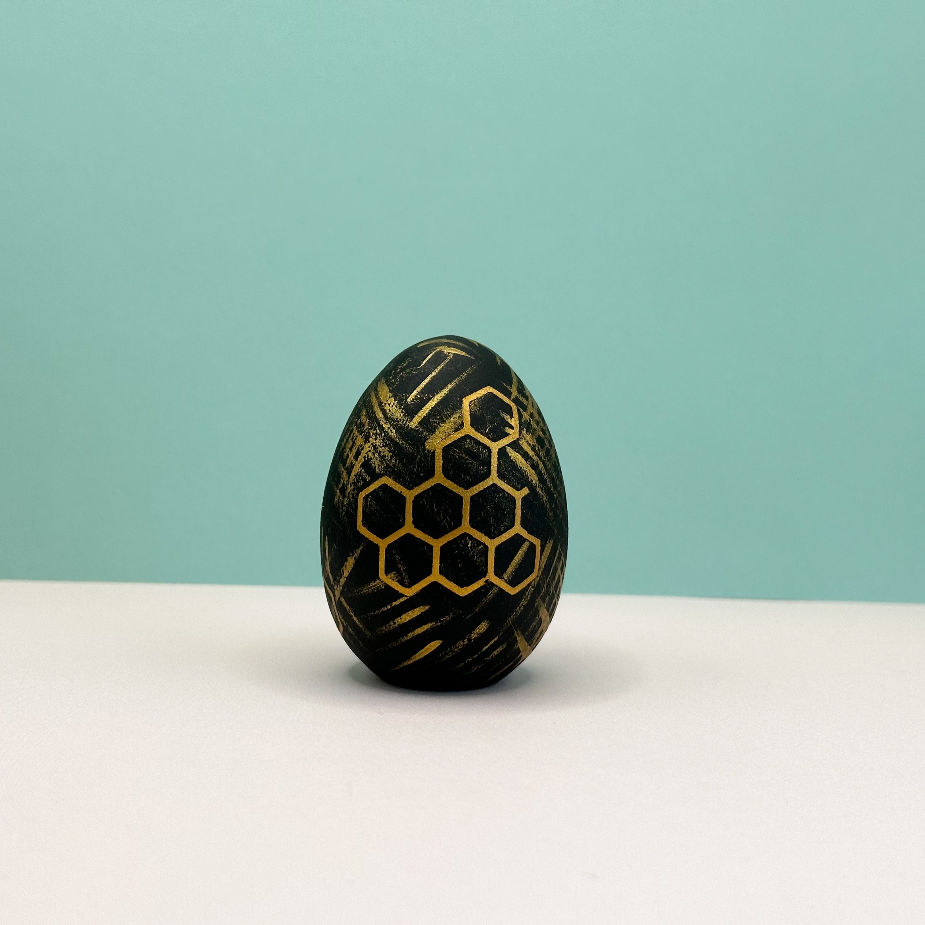 Black egg with gold honeycomb pattern on a white surface and light blue background