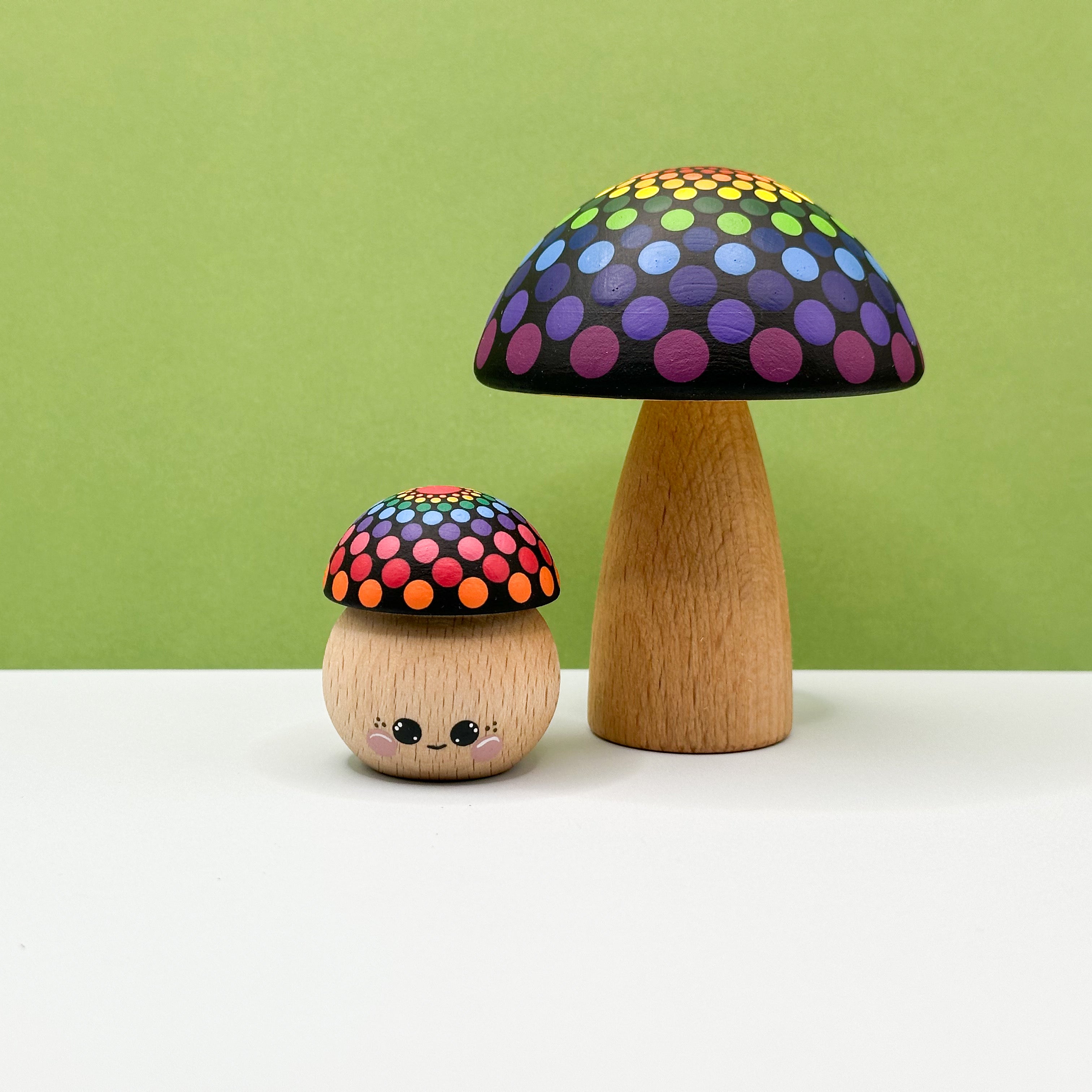 Two wooden mushroom toys with colorful polka dot caps on a white surface against a green background