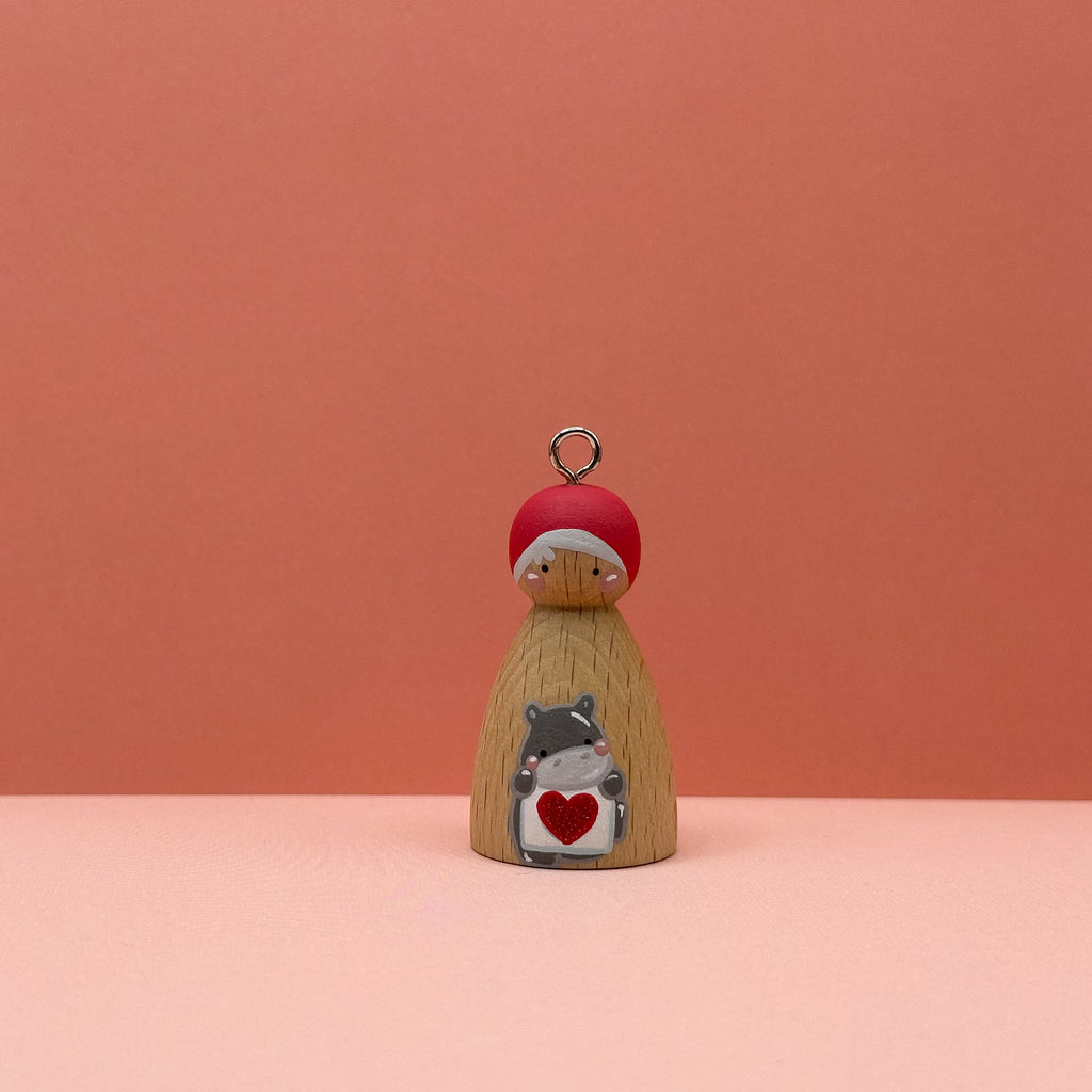 Small peg doll keyring with a hippo holding a heart sign painted on its body with a peach background