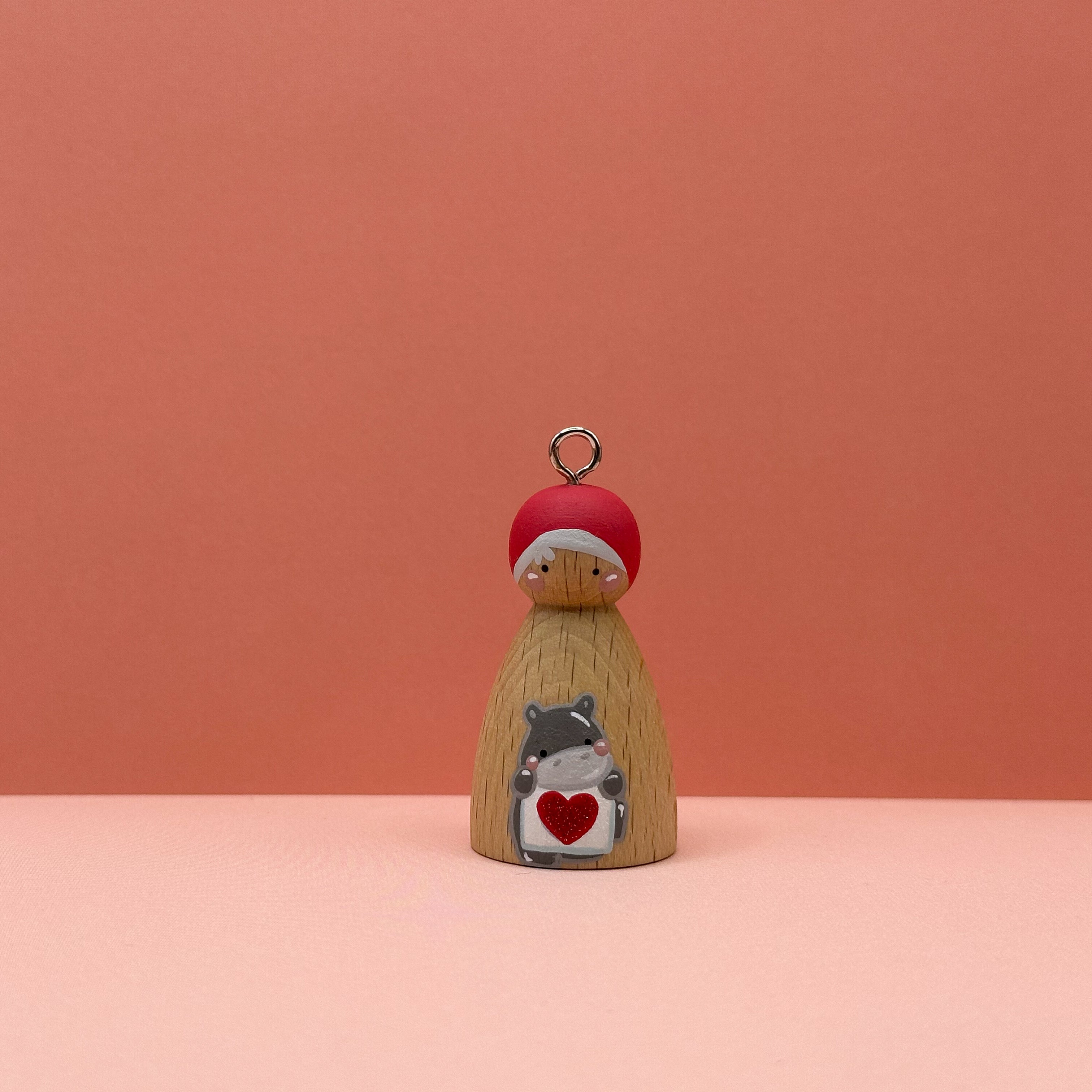 Small peg doll keyring with a hippo holding a heart sign painted on its body with a peach background