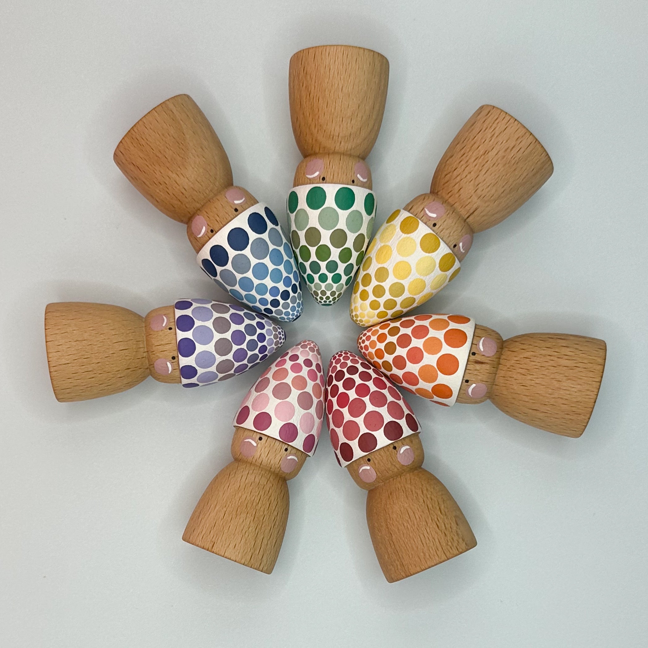 Wooden dolls with colorful polka dot patterns on a light gray background