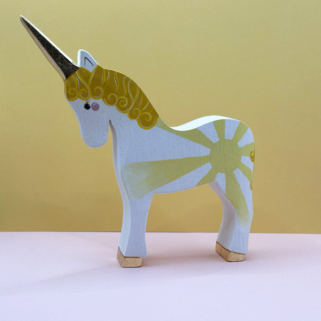 Wooden unicorn figurine with gold and yellow design on a beige background