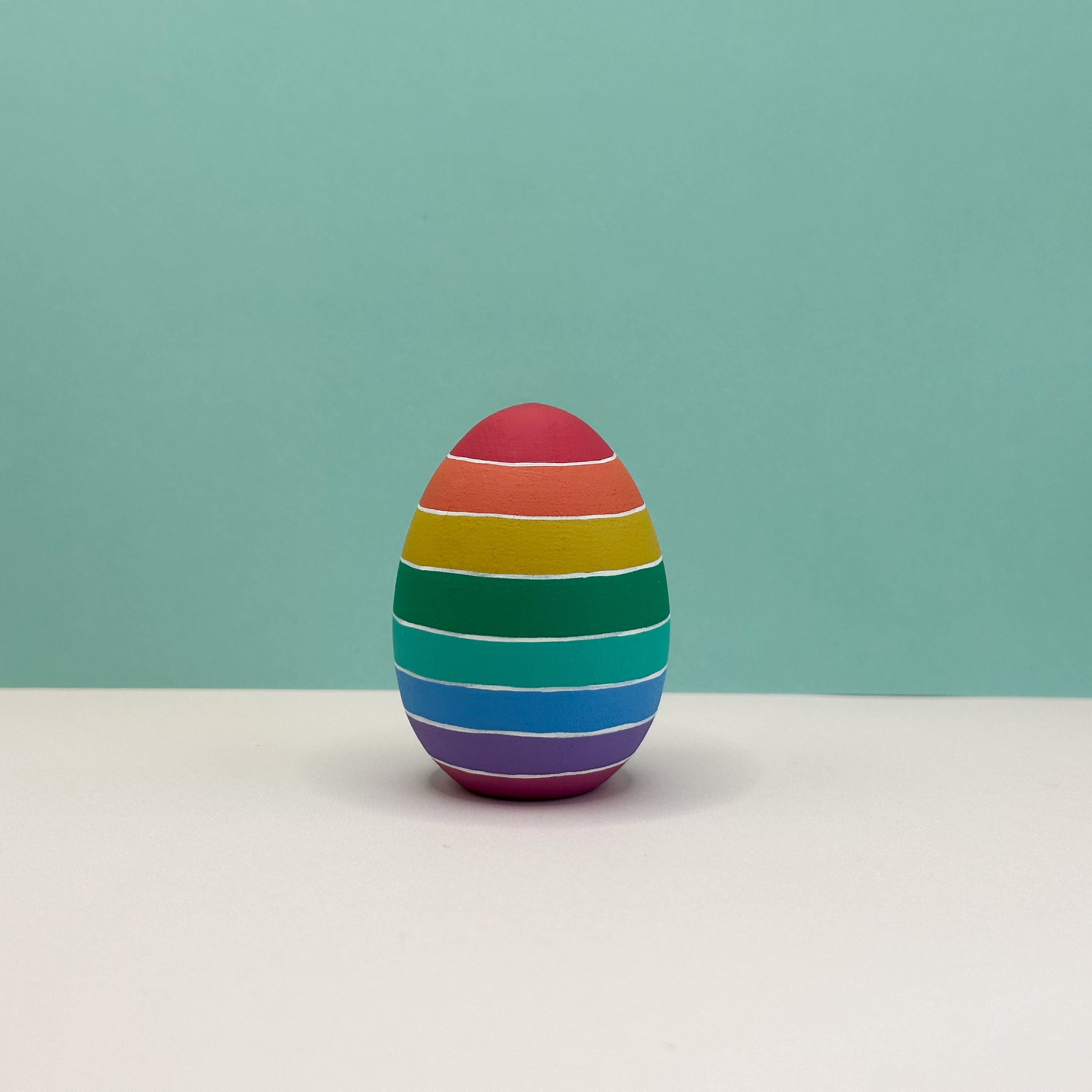 Colorful striped egg-shaped object on a light surface with a light green background