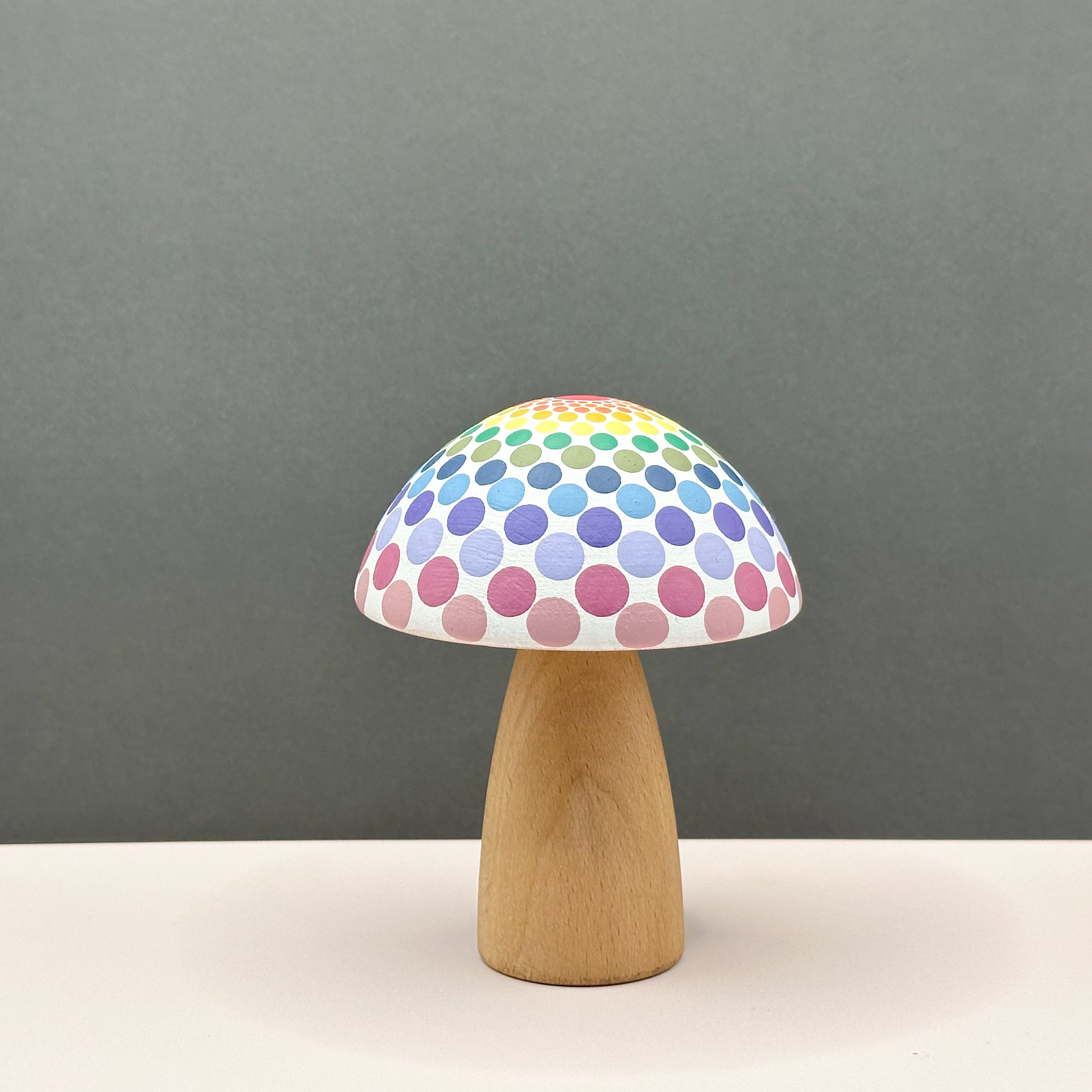 Mushroom-shaped wooden toy with a colorful polka dot design on a gray background