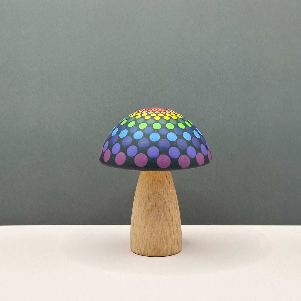 Mushroom-shaped wooden toy with a colorful polka dot design on a wooden base against a gray background