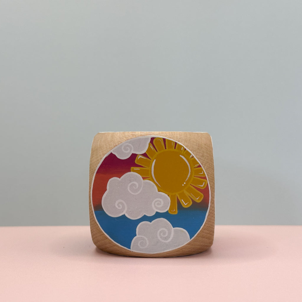 Wooden block with a colorful sun and cloud design on a gray background