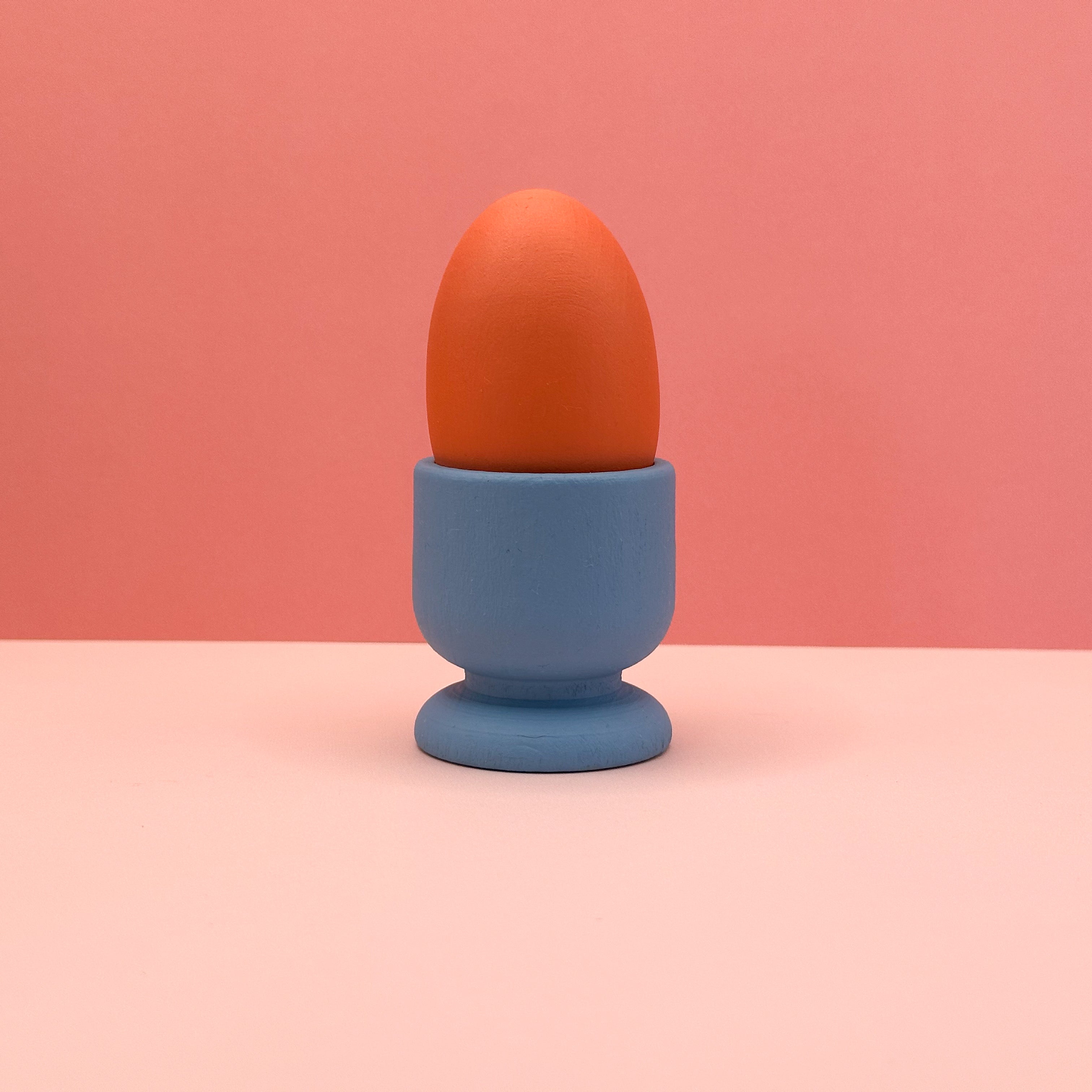 Orange egg in a blue holder on a pink background
