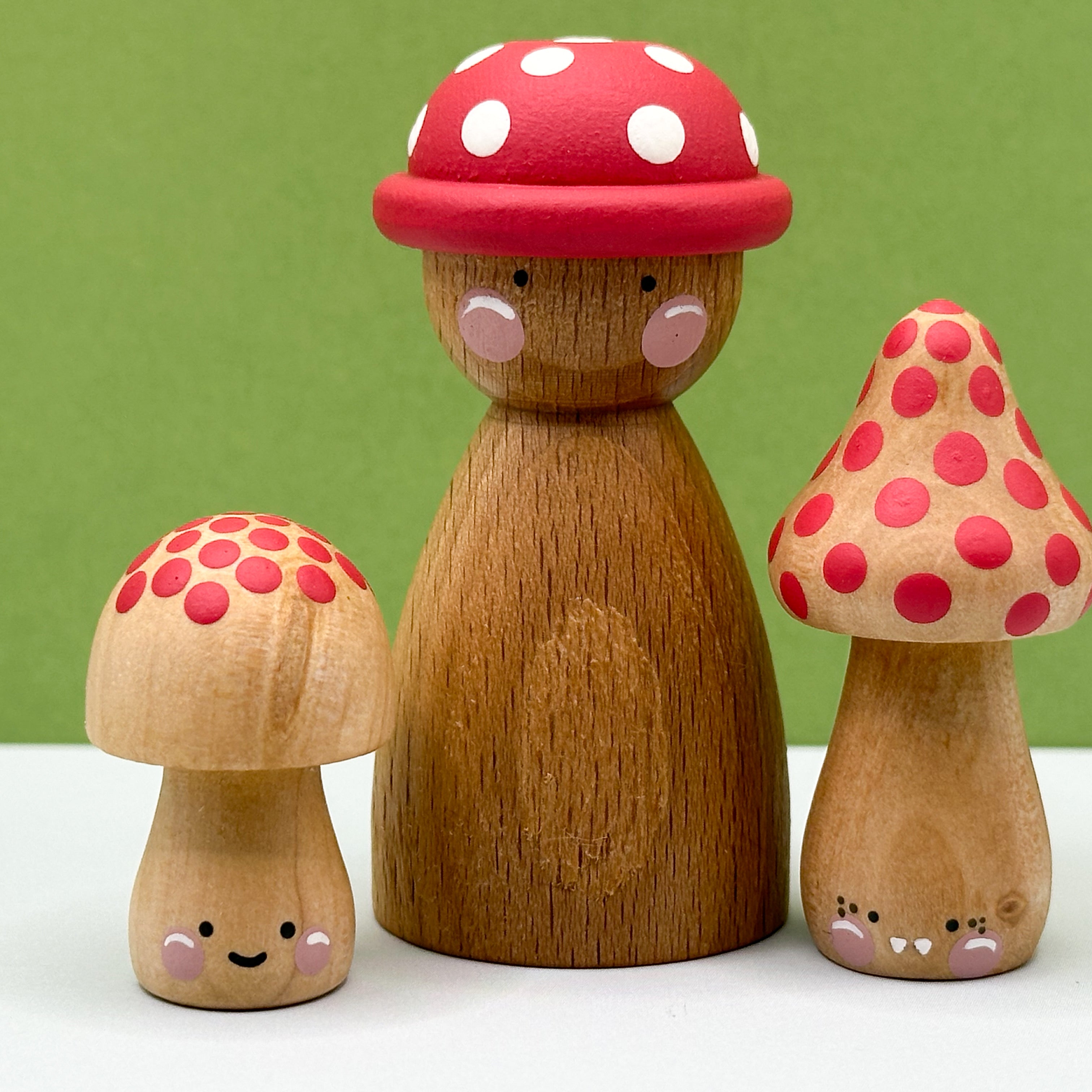 Wooden peg doll with red polka dot mushroom hats on a white surface with green background