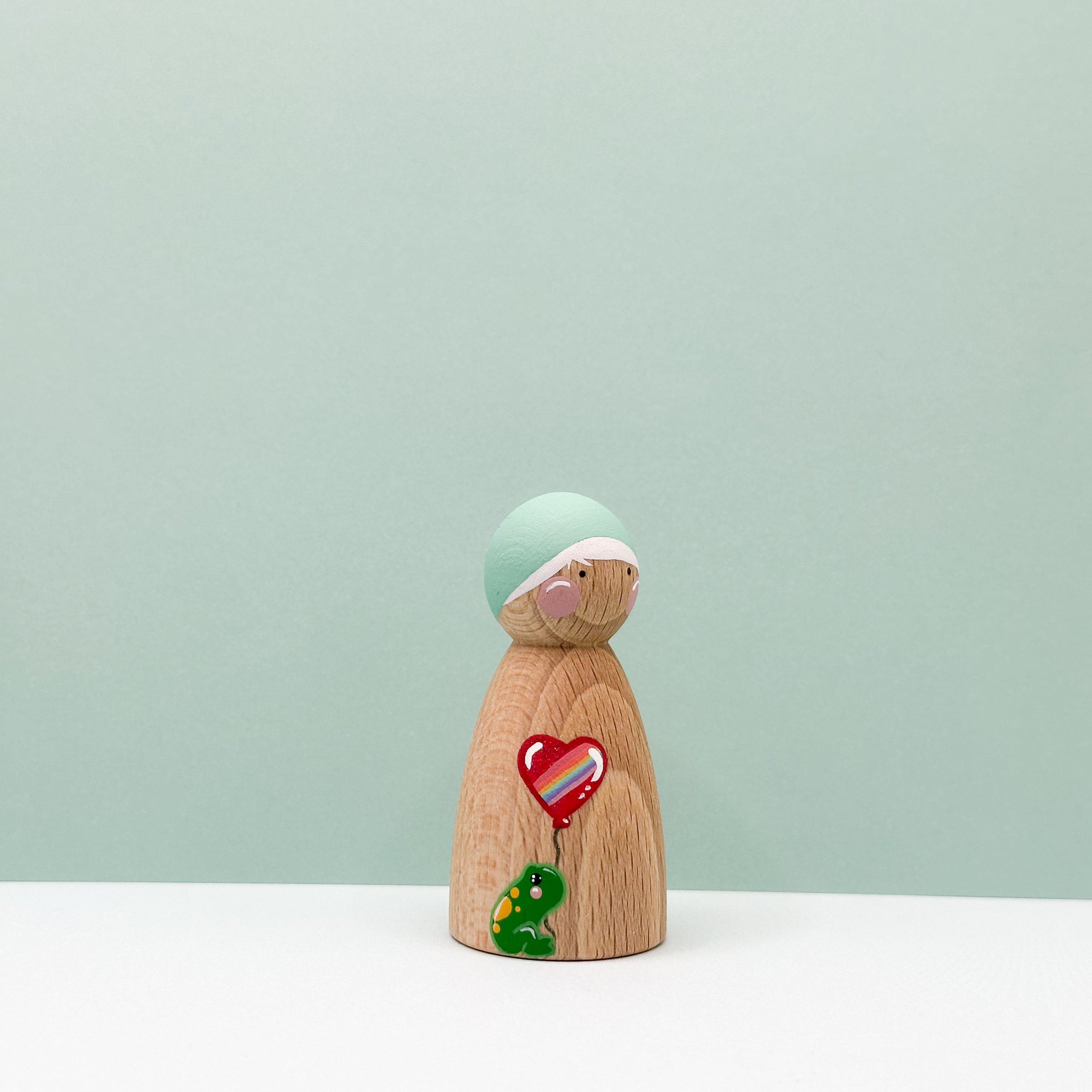 Wooden figurine with a green hat and heart-shaped balloon on a light green background