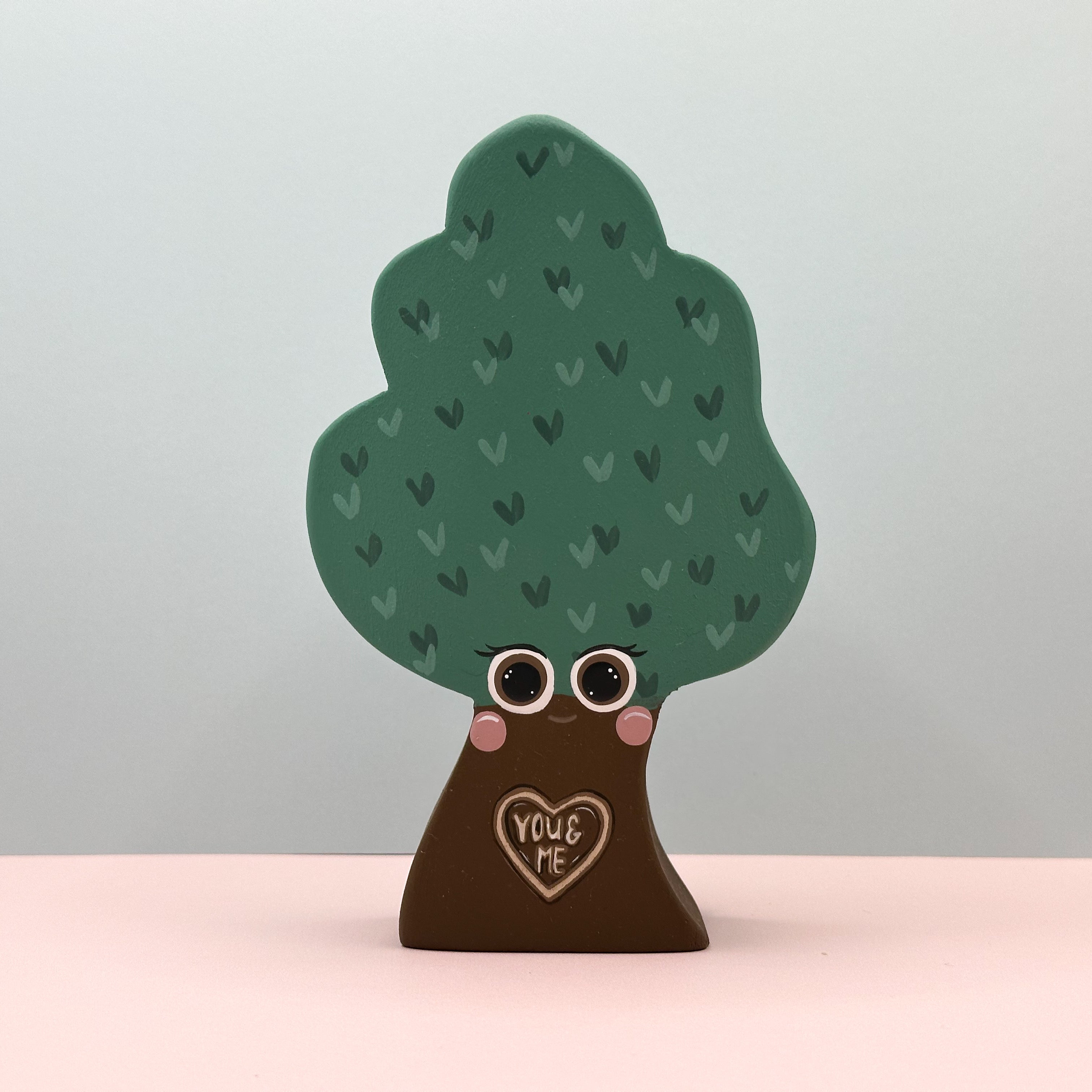 Decorative tree-shaped figurine with eyes, heart, and 'You & Me' text on a plain background