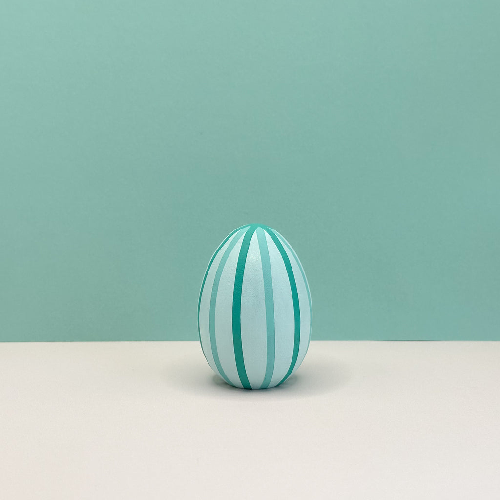 Decorative egg with green stripes on a light beige surface and teal background
