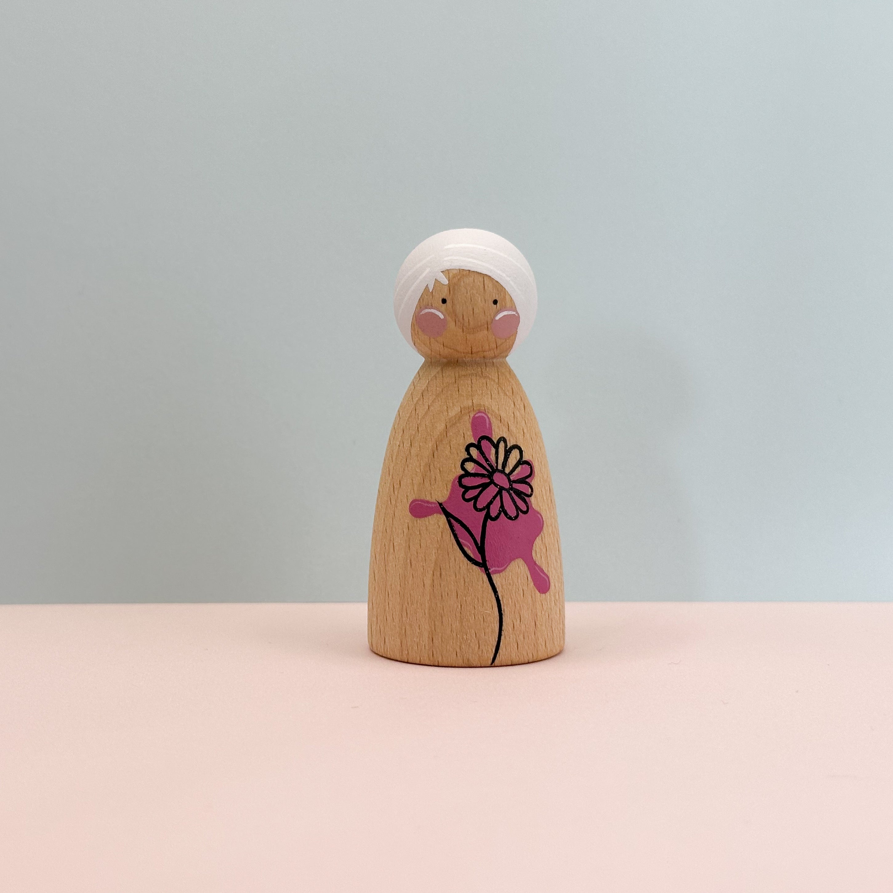 Wooden peg doll with a pink flower design on a light gray background