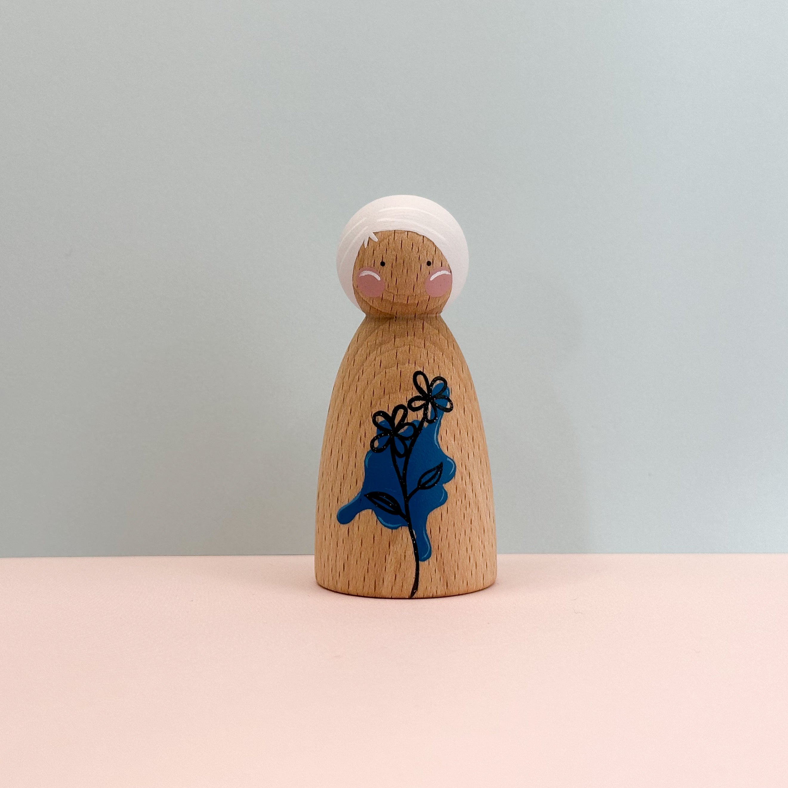 Wooden peg doll with a blue flower design on a light gray background