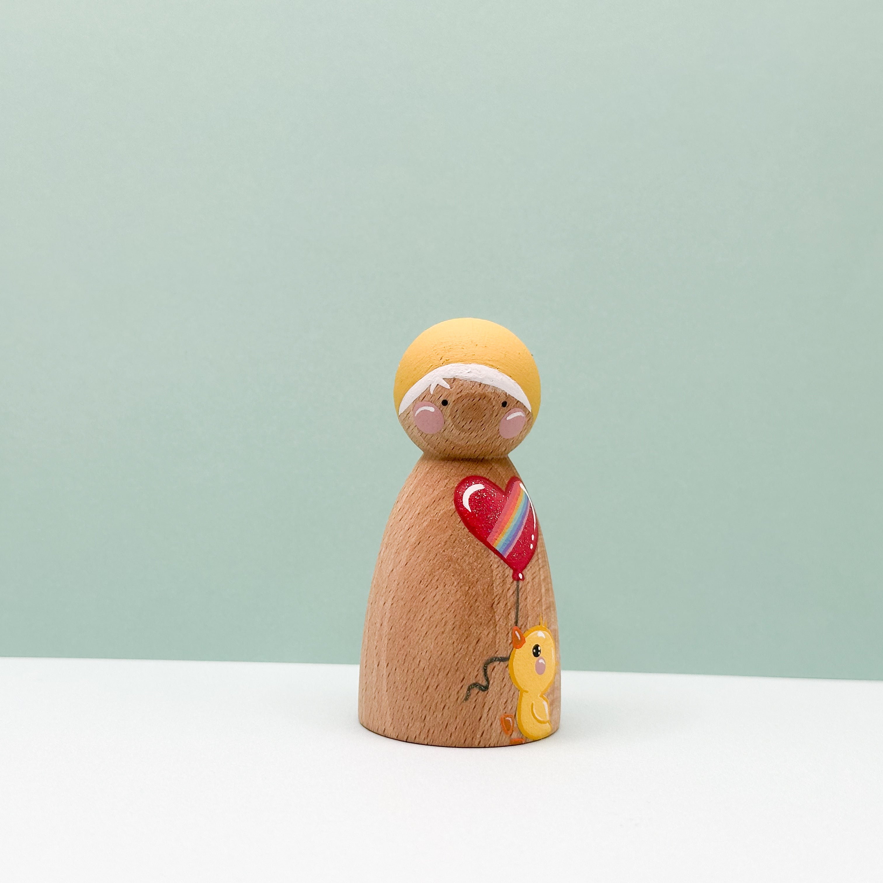 Wooden peg doll with a heart-shaped balloon on a light green background