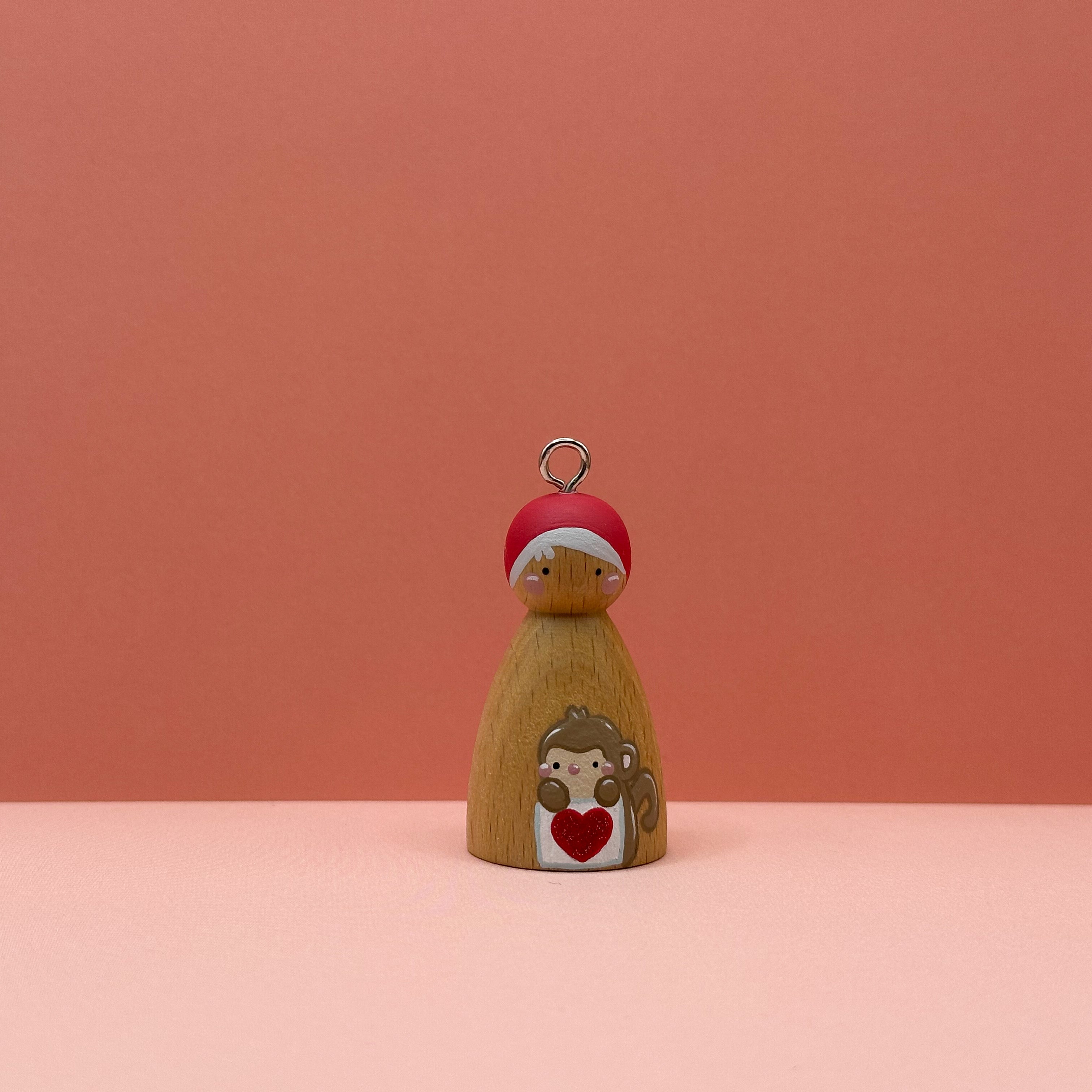Small peg doll keyring with a Monkey holding a heart sign painted on its body with a peach background