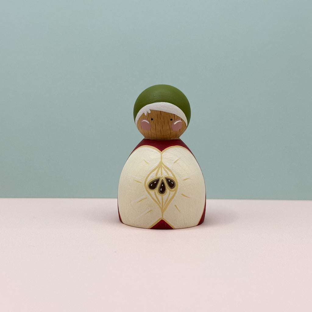Wooden figurine with a green hat and red and white apple body on a light blue background