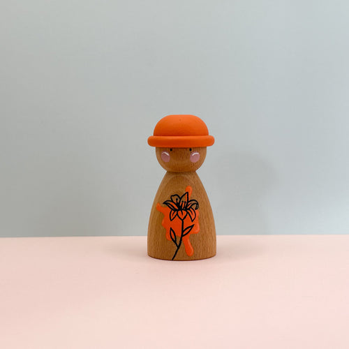Wooden peg doll with an orange hat and black floral design on a light gray background