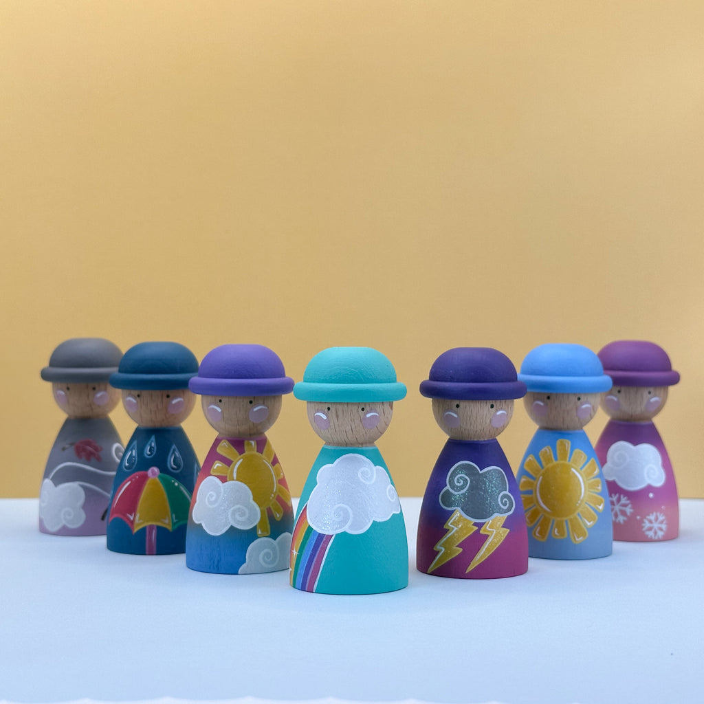 Set of colorful wooden peg dolls with weather theme on a white surface against a yellow background
