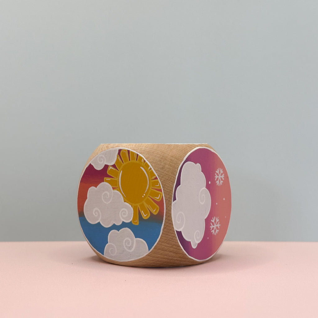 Wooden toy with colorful painting of a sun and clouds on a pink surface.
