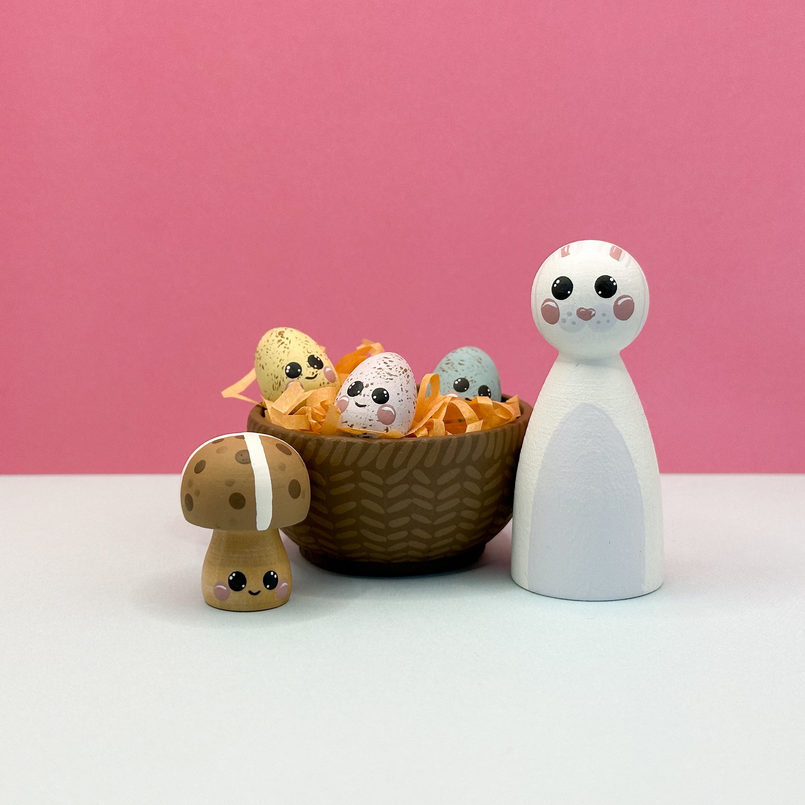 Set of small figurines including a mushroom, eggs, and a rabbit-like figure on a pink background