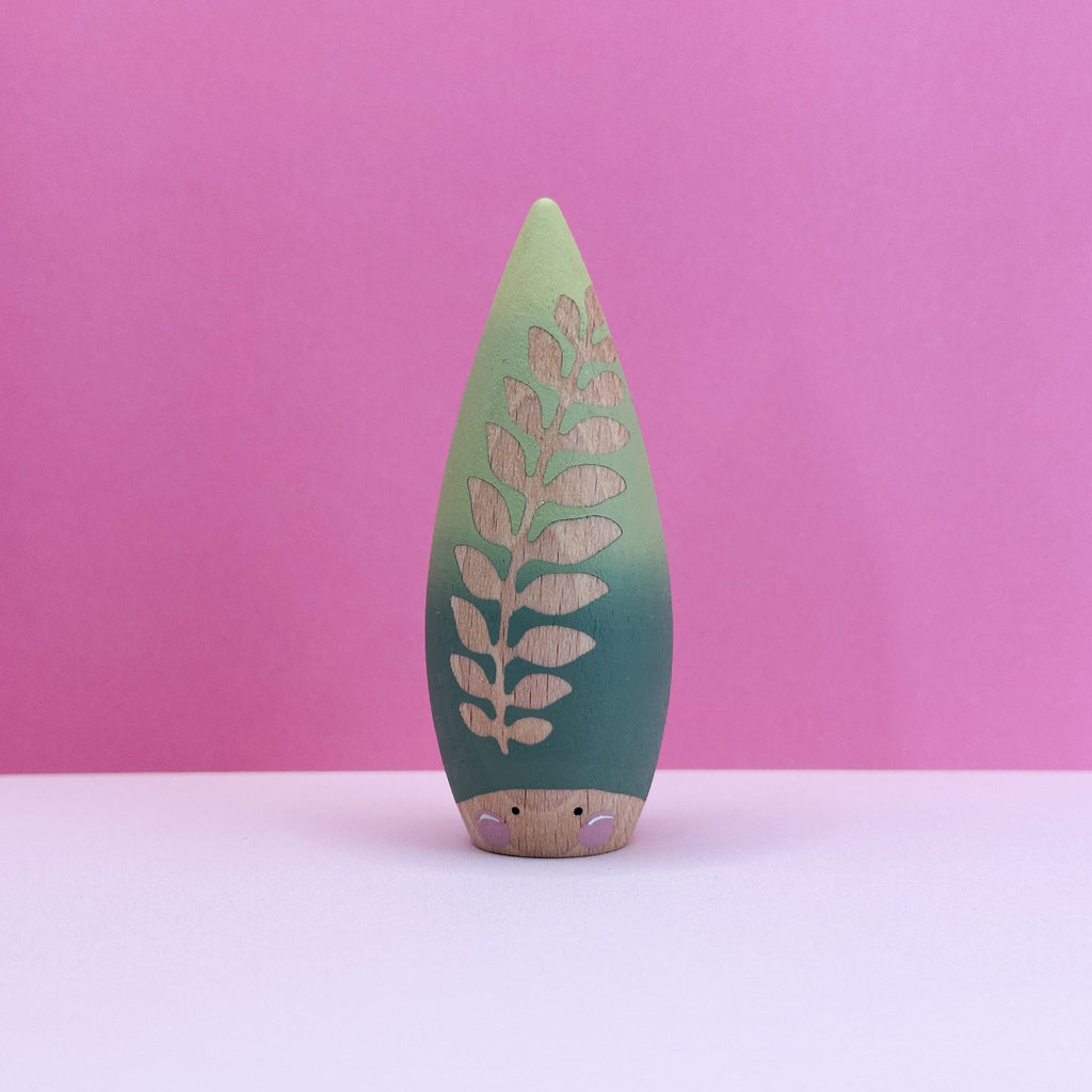 Wooden toy shaped like a teardrop with a leaf with cut-out design on a pink background