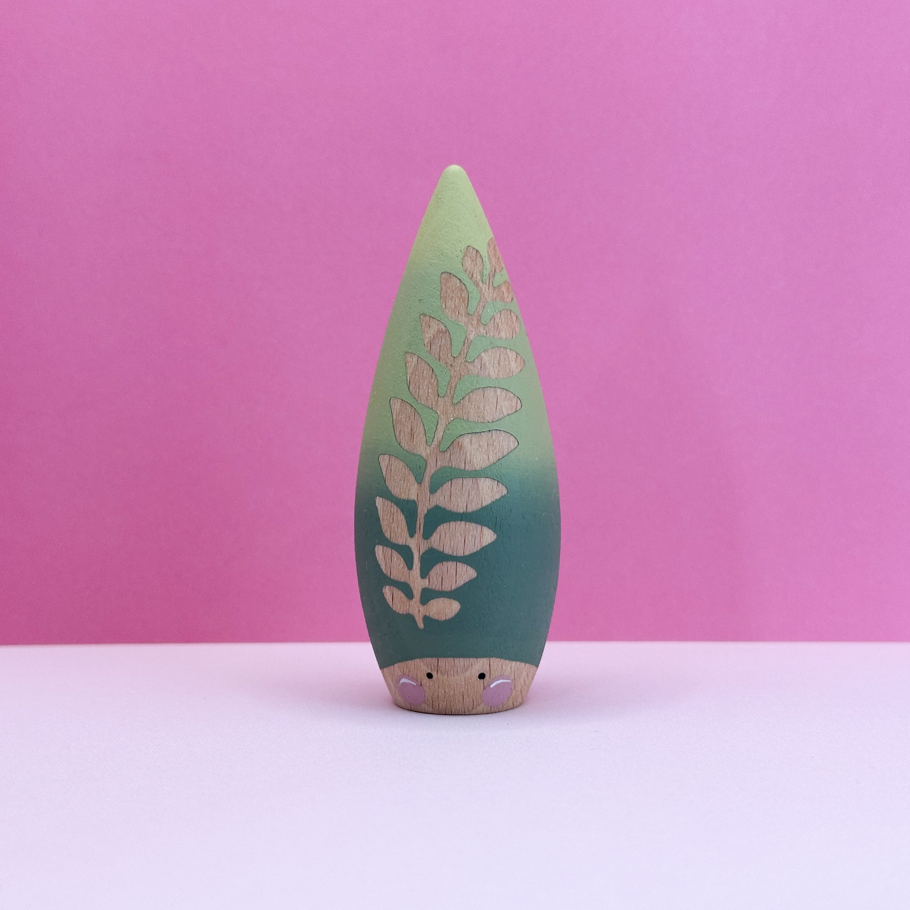 Wooden toy shaped like a teardrop with a leaf with cut-out design on a pink background