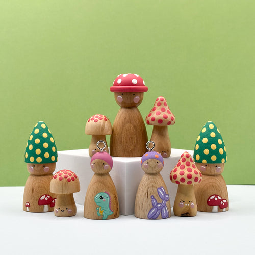 Wooden peg dolls with colorful mushroom hats on a white surface against a green background