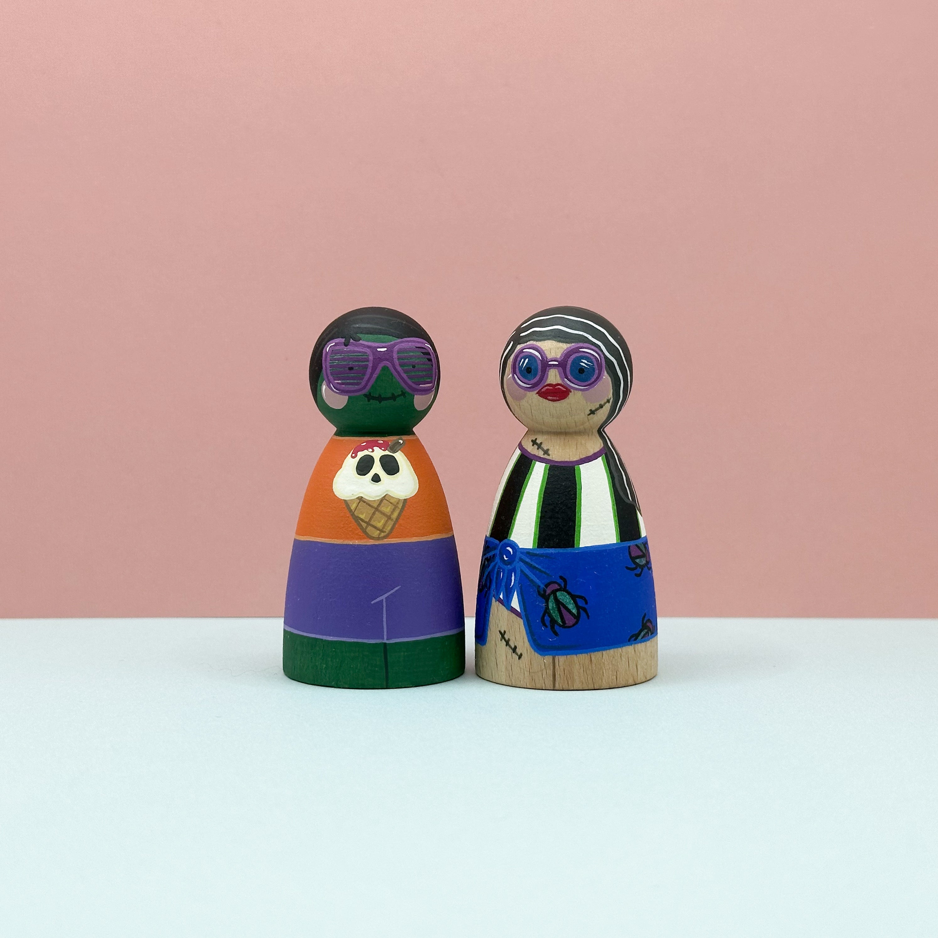 Two colorful wooden peg dolls with sunglasses on a pink background