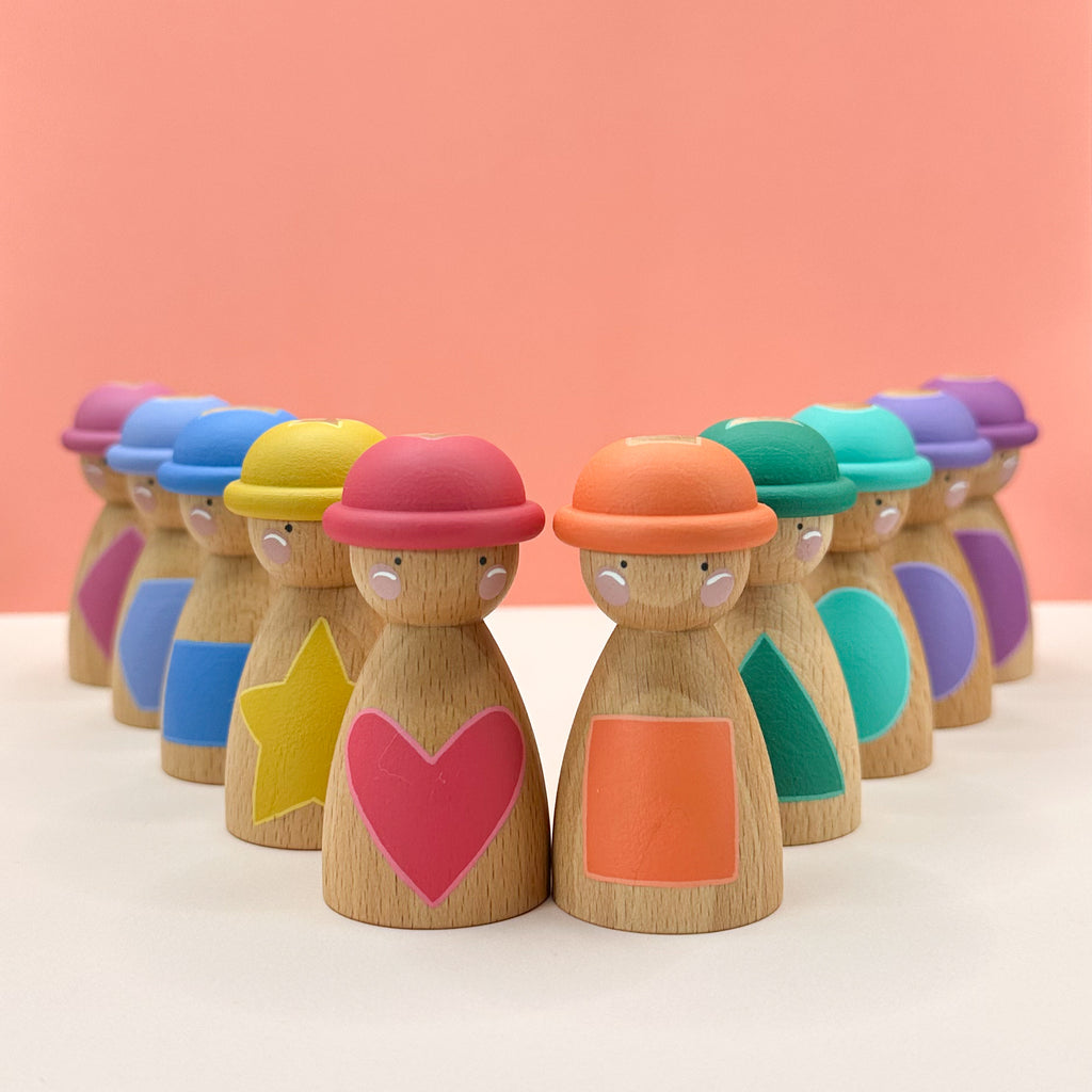 Row of colorful wooden peg dolls with different hats and painted shapes on their tummies on a peach background