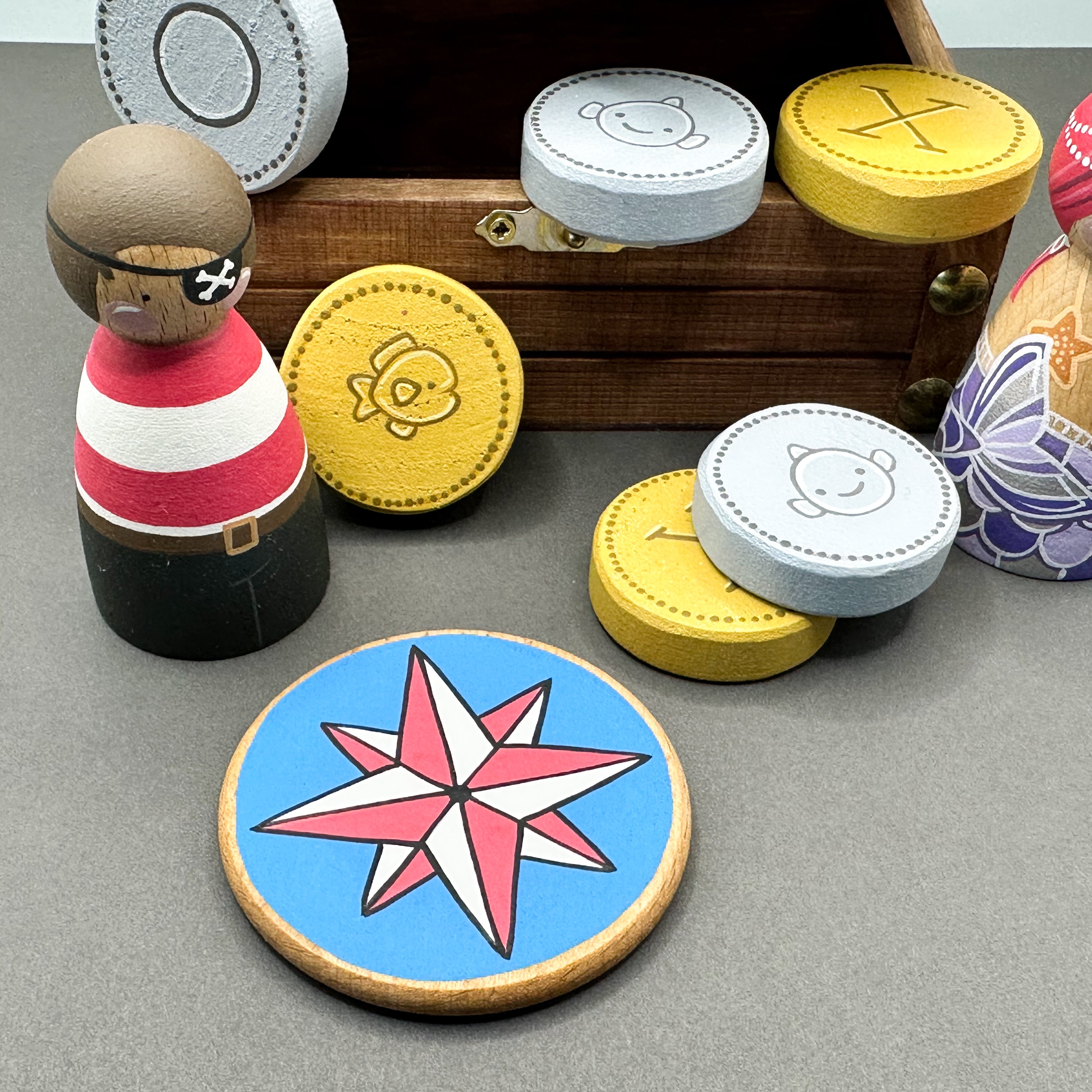 Wooden toy treasure chest with wooden peg dolls, wooden coins and a round disc shaped treasure map