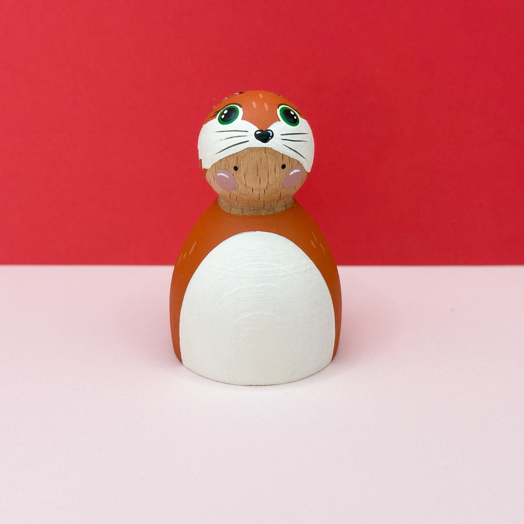 Wooden toy figure of a fox on a pink surface with a red background