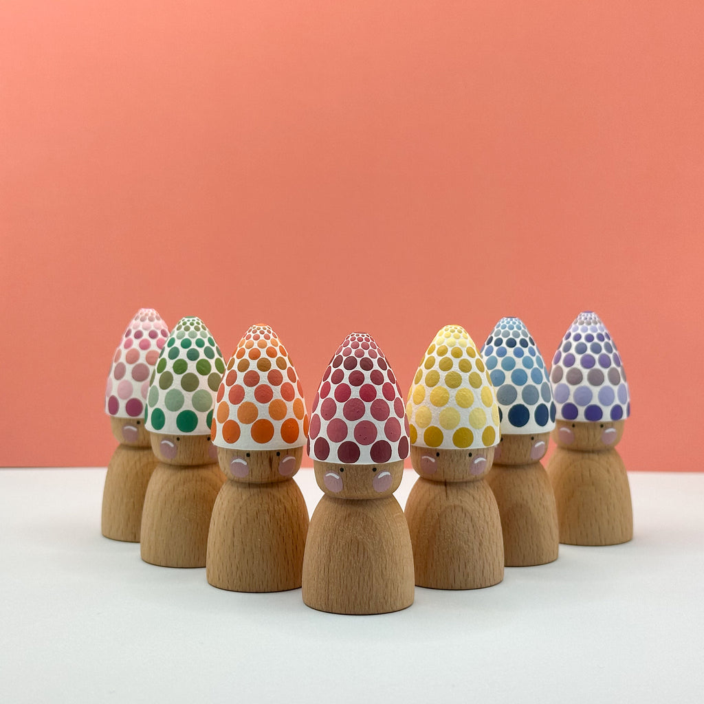 Wooden peg dolls with colorful polka dot hats on a white surface and peach background