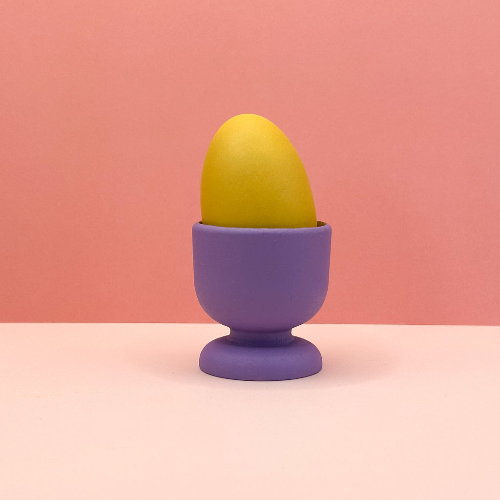 Yellow egg in a purple egg cup on a pink background